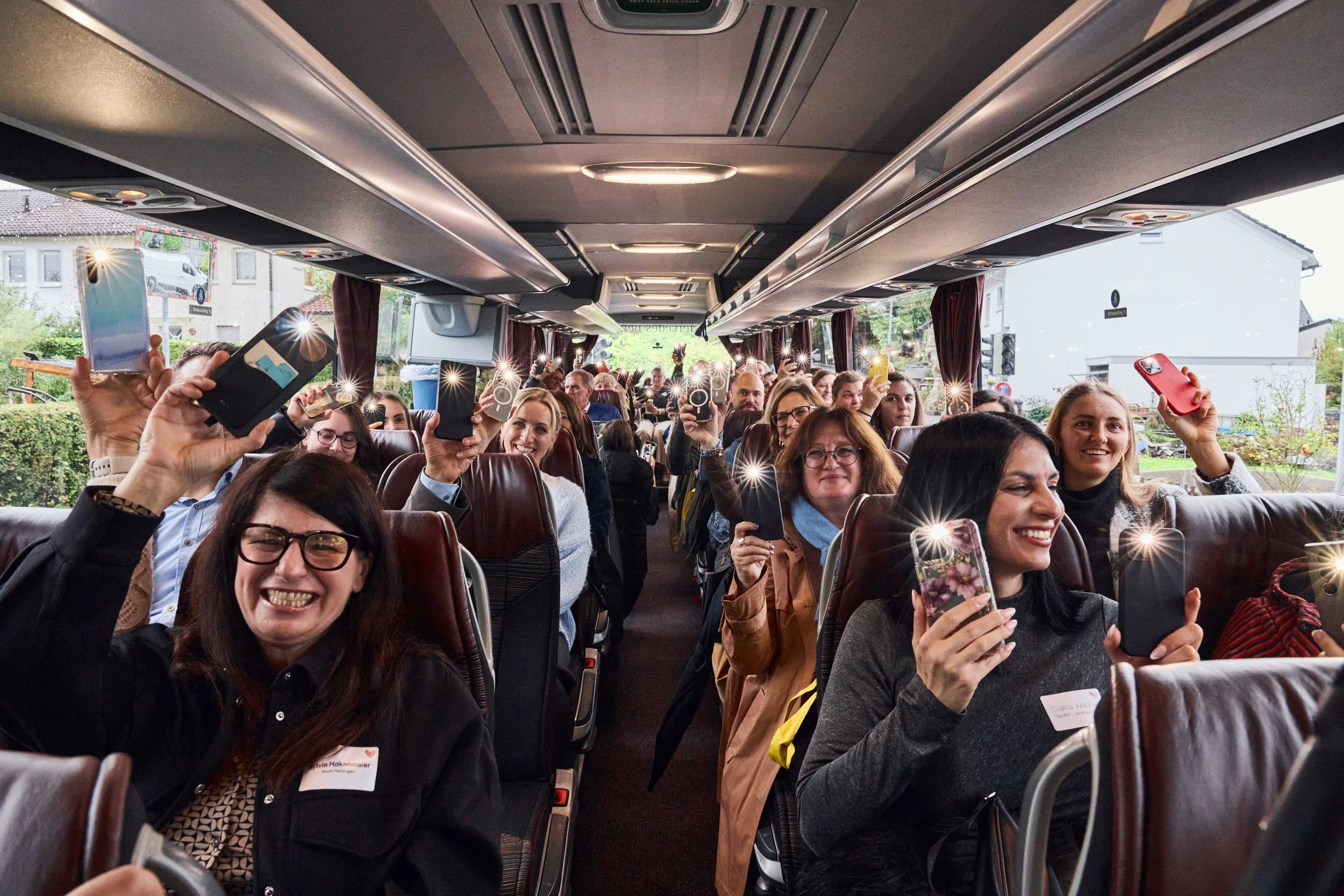 Menschen auf einem Reisebus sitzen und Fotos mit ihren Handys machen, lachen und genießen, während sie sich auf eine Reise oder Veranstaltung vorbereiten.