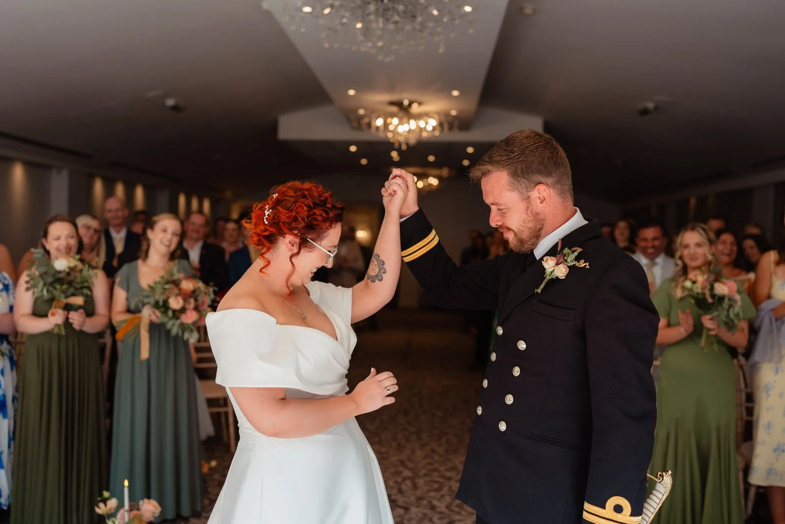 Celebrating wedding couple, holding each others hands in the air celebrating their vows amongst wedding guests clapping behind them. In the ceremony room at the Bear Hotel in Cowbridge.