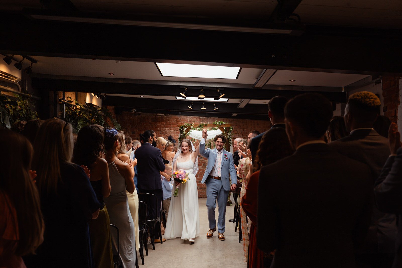 Excited wedding couple walking back down the aisle to cheers after getting married, inside the Shack Revolution Hereford