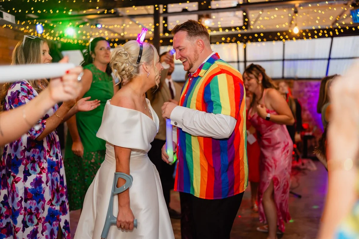 Dancefloor scene, wedding couple dancing, male in a bright multi coloured stripe shirt, bride with a flashing tiara on. Wedding guests dancing around them.