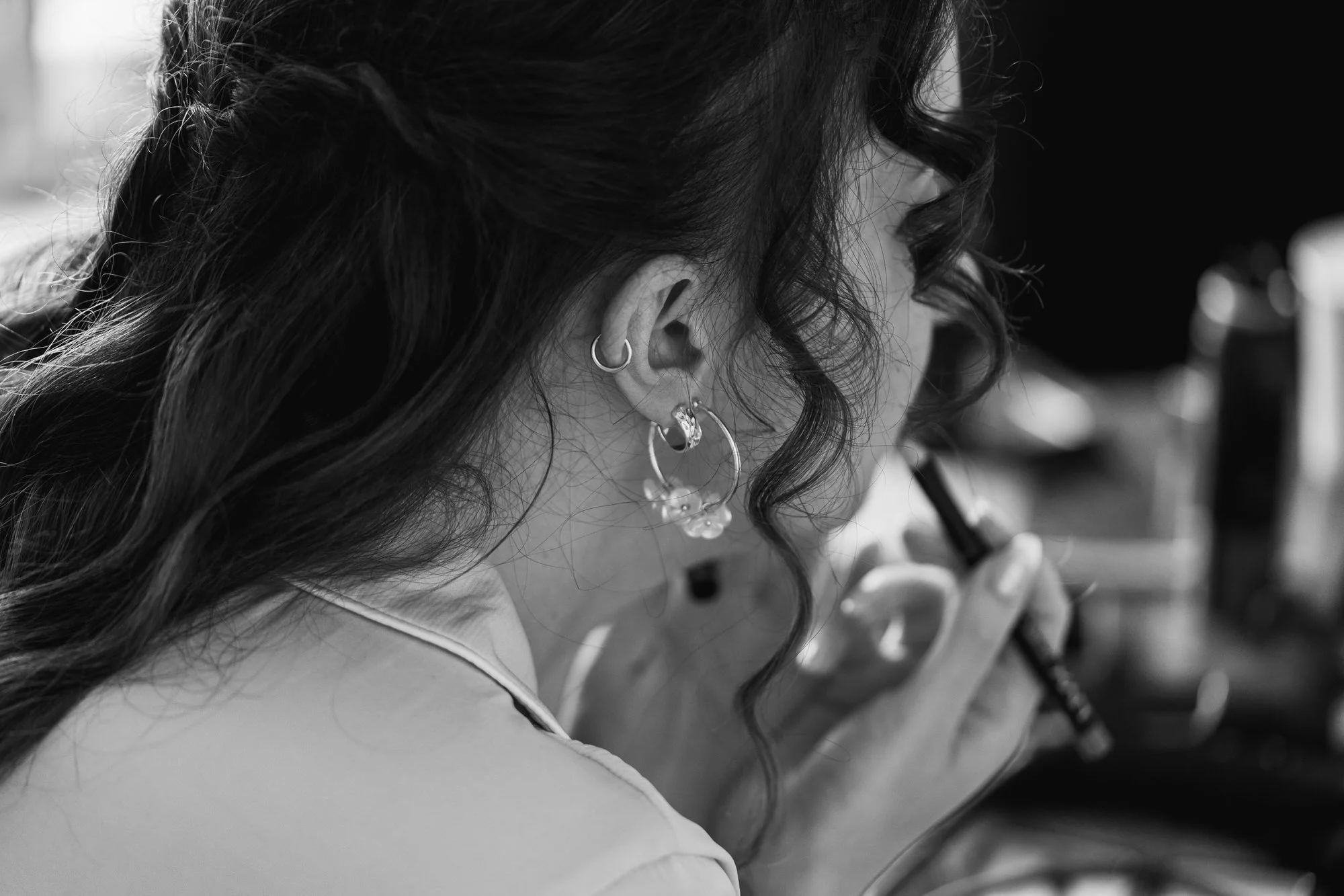 A woman applies lip liner in front of a mirror, her hands and face partially visible in black and white.
