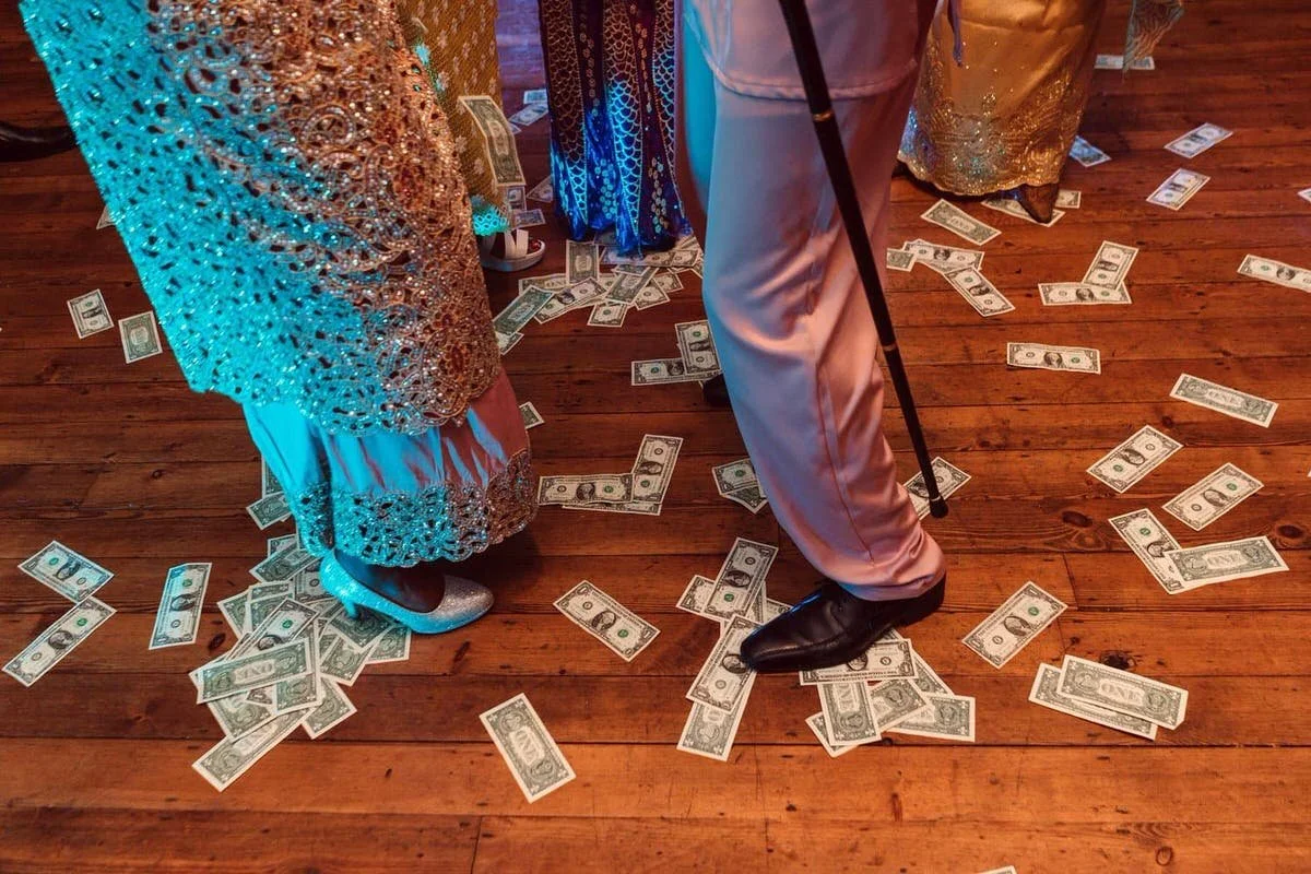 African bride and groom in traditional colourful sparkly dress dancing over a scattering of dollar bills on the floor.