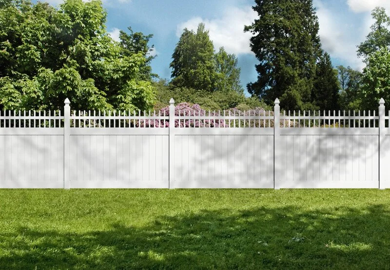 White picket fence with a grassy yard, trees, and blue sky in the background.