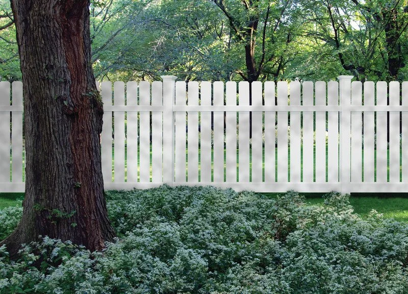 A backyard with a well-maintained green lawn, a white privacy fence running along the edge, and trees in the background, with a portion of a house visible on the left.