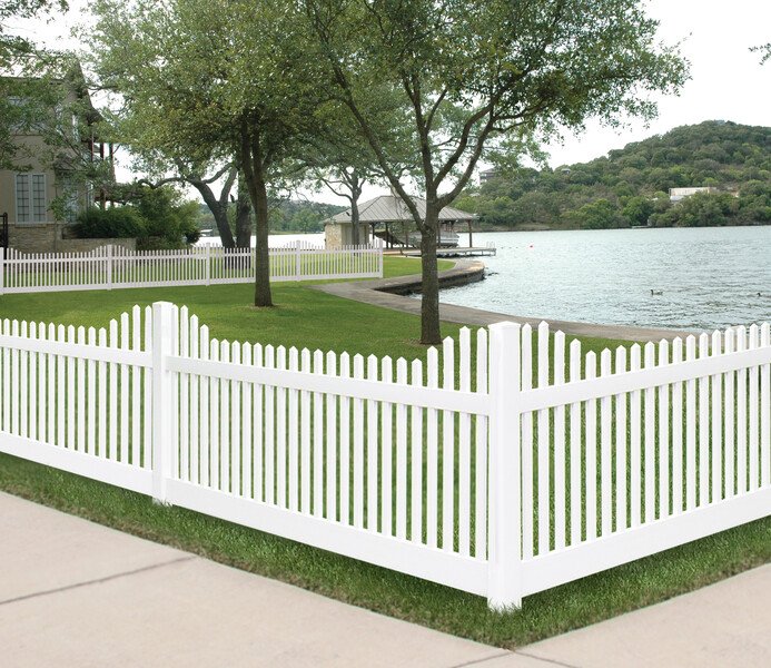 White picket fence surrounding a grassy area with trees near a lake, with a gazebo and ducks in the water.