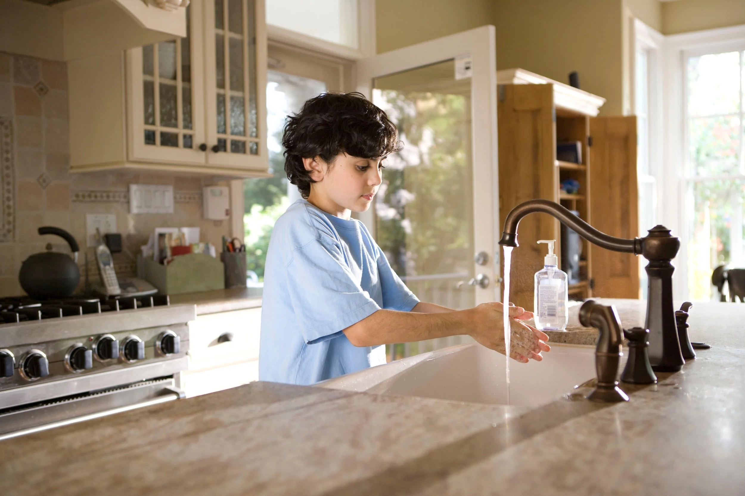 A young boy washing his hands in a kitchen