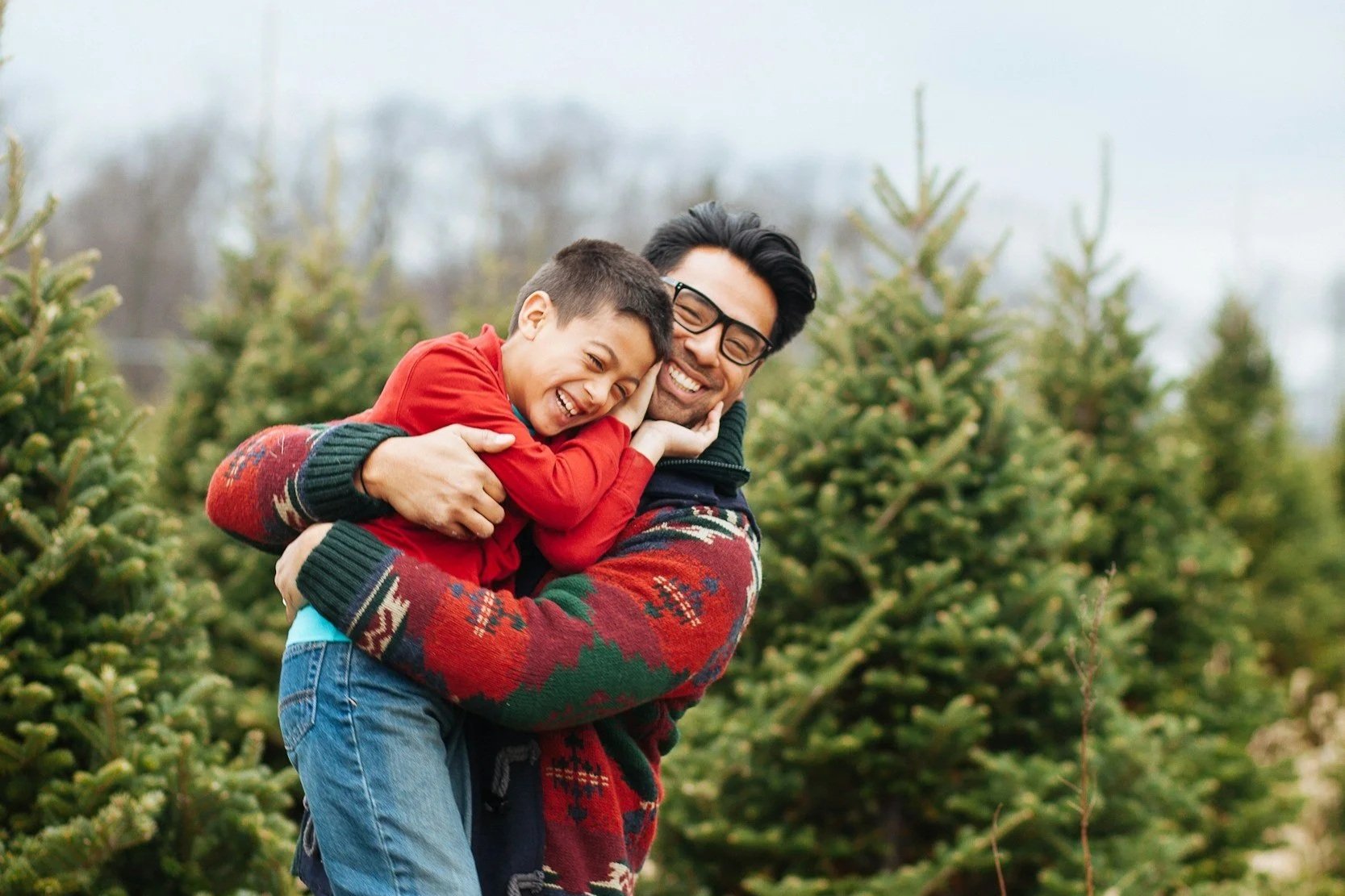 a man and male child embracing by pine trees