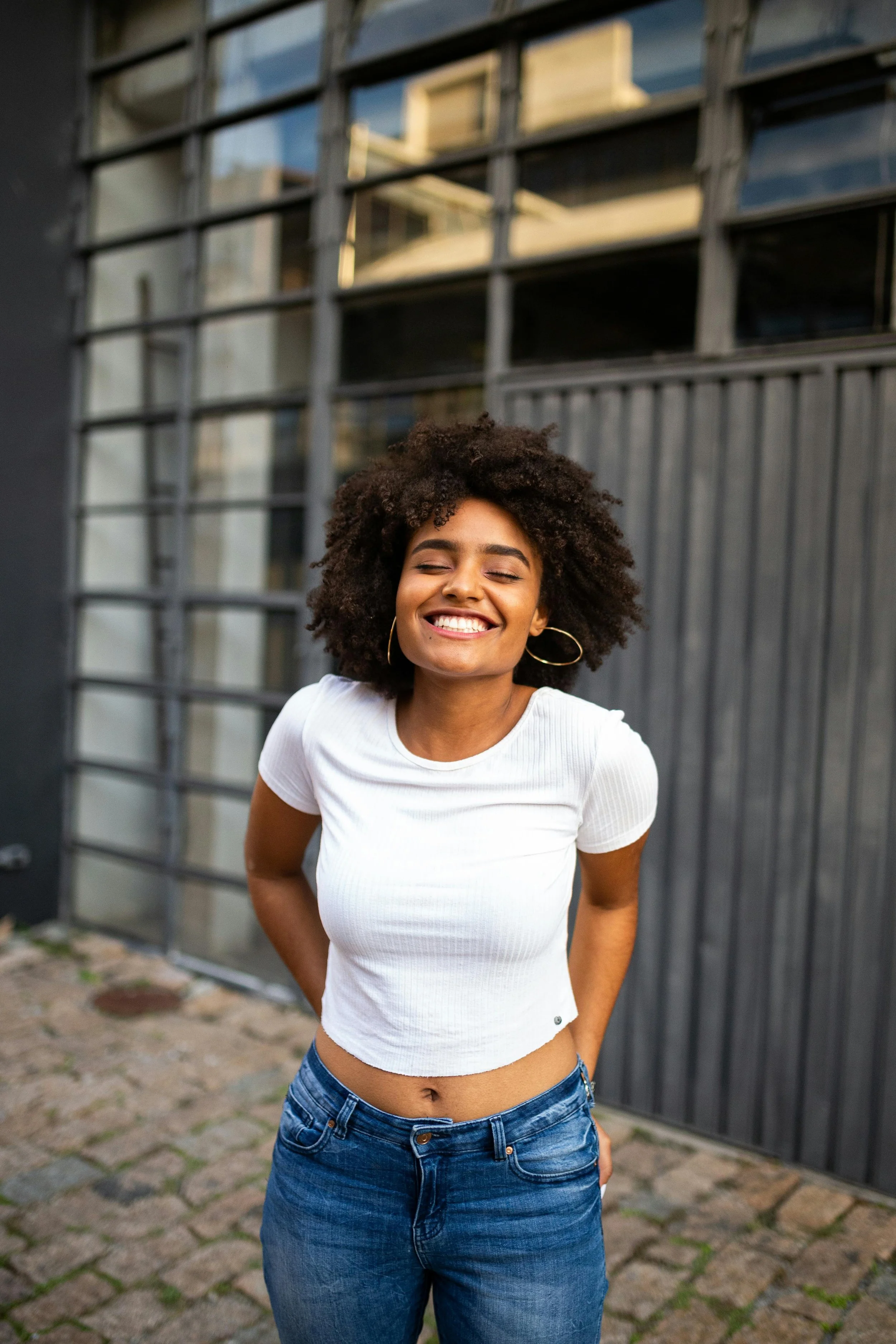 a smiling Black woman in a white top and denim jeans outdoors