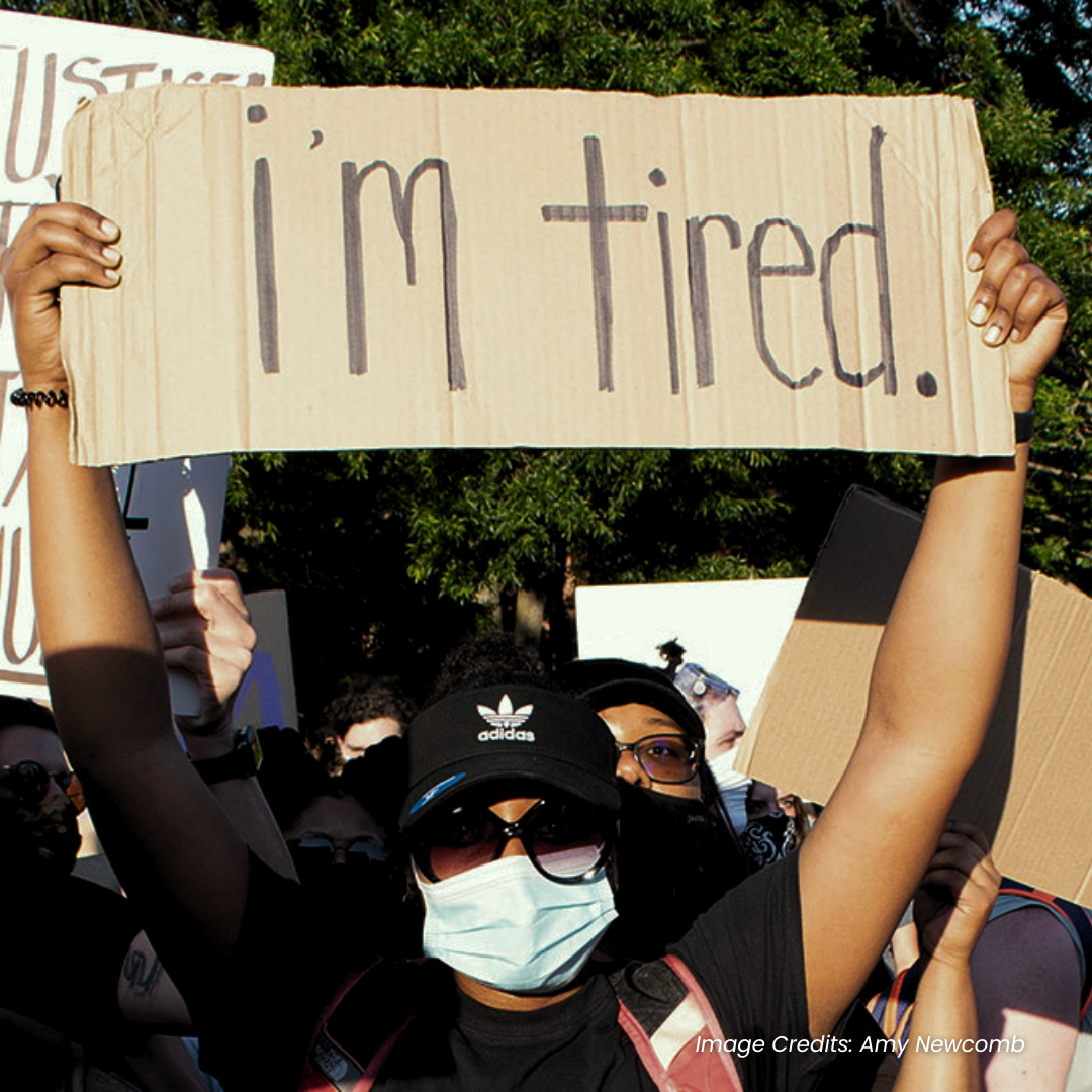 A protestor holding a placard saying "I'm tired."