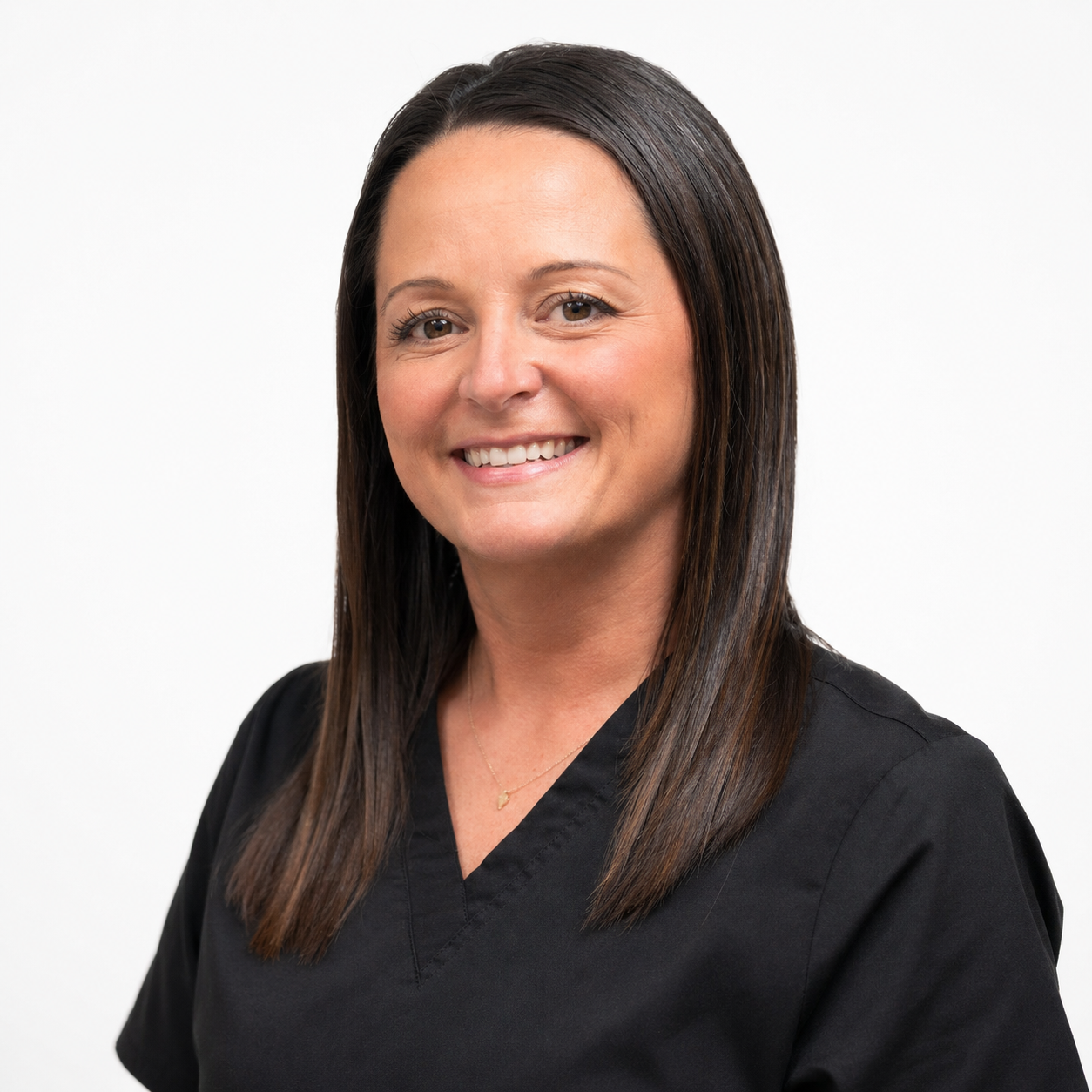 Portrait of a woman with straight dark brown hair, smiling, wearing a black medical uniform, and a delicate gold necklace, against a white background.