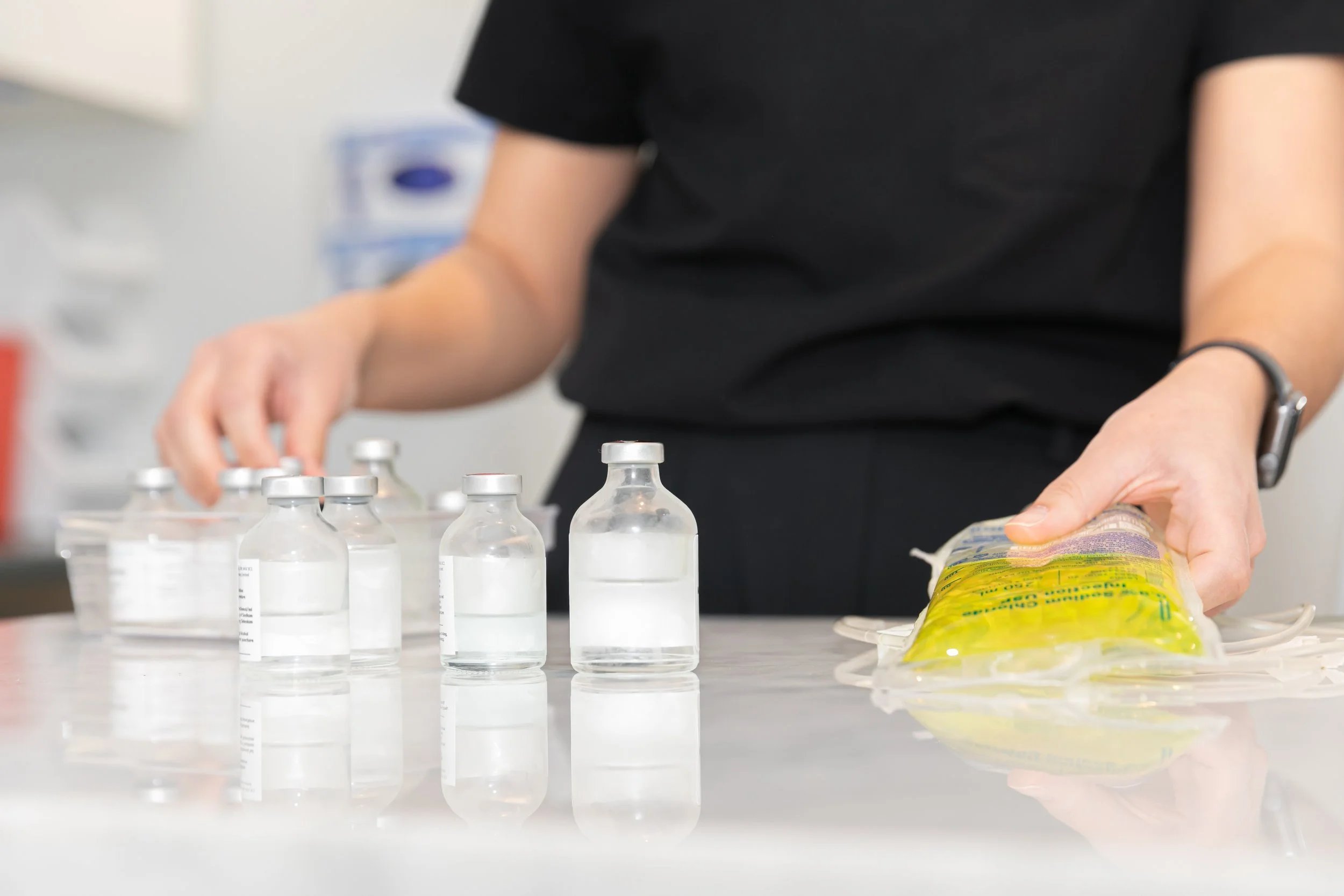 A practitioner  holding an IV bag with vials of medication on a white counter 