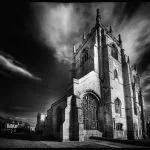 The Minster, King's Lynn.  A dark, ominous church with Gothic architecture and a tall, pointed steeple under a stormy sky.