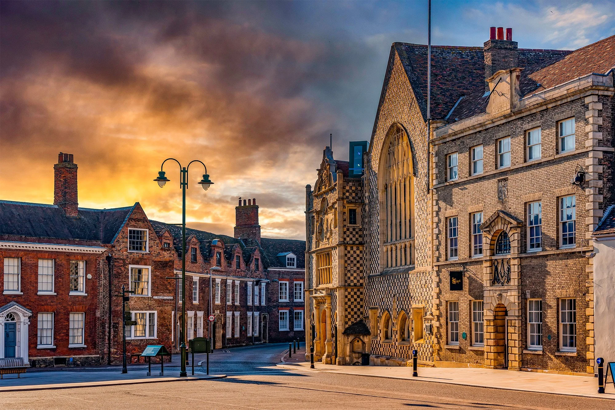 Saturday Market Place, King's Lynn.  Historic brick and stone buildings on a quiet street at sunset with a cloudy sky.