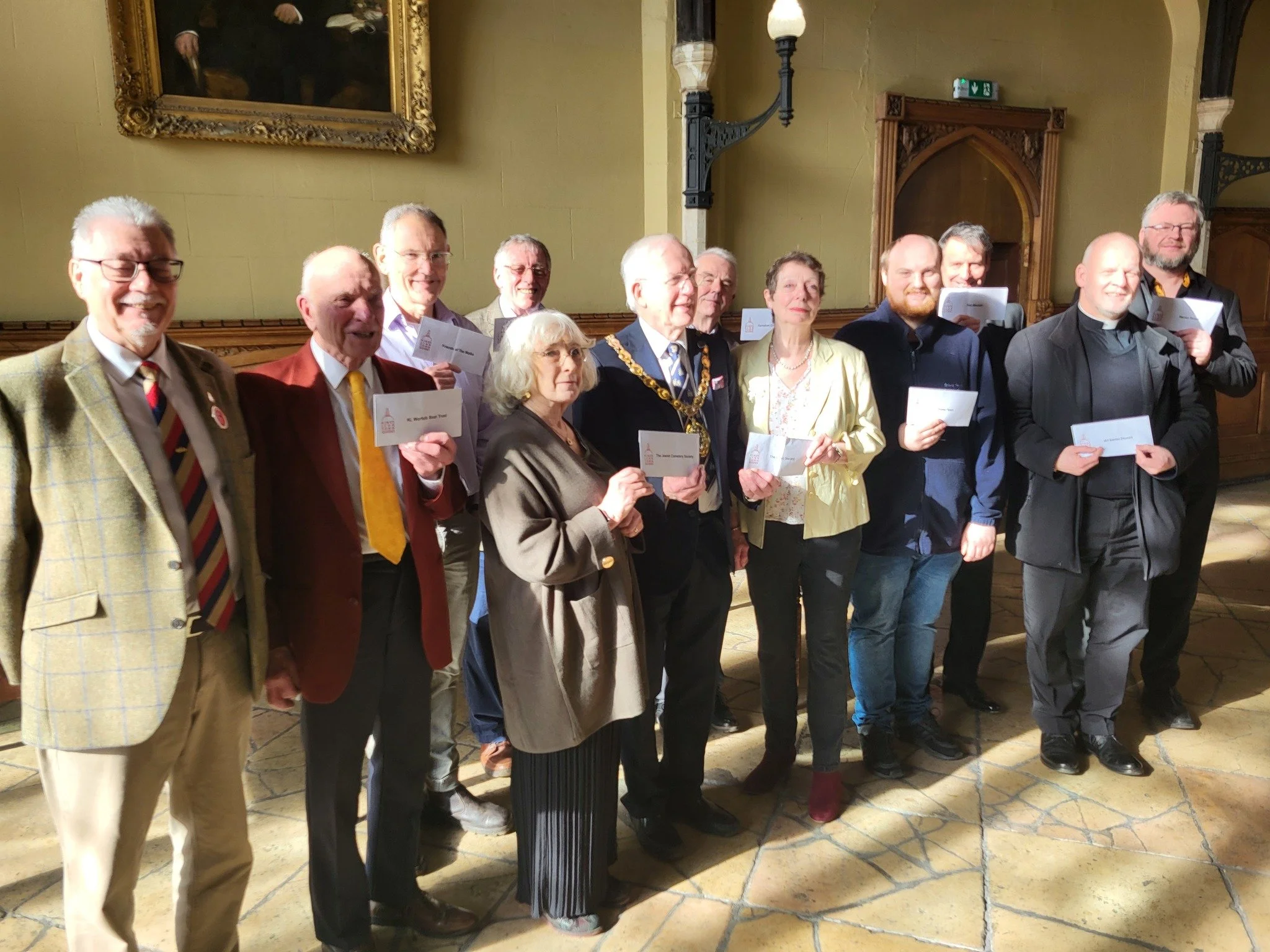 Group of people in formal attire celebrating awards ceremony in a historic hall, holding certificates.