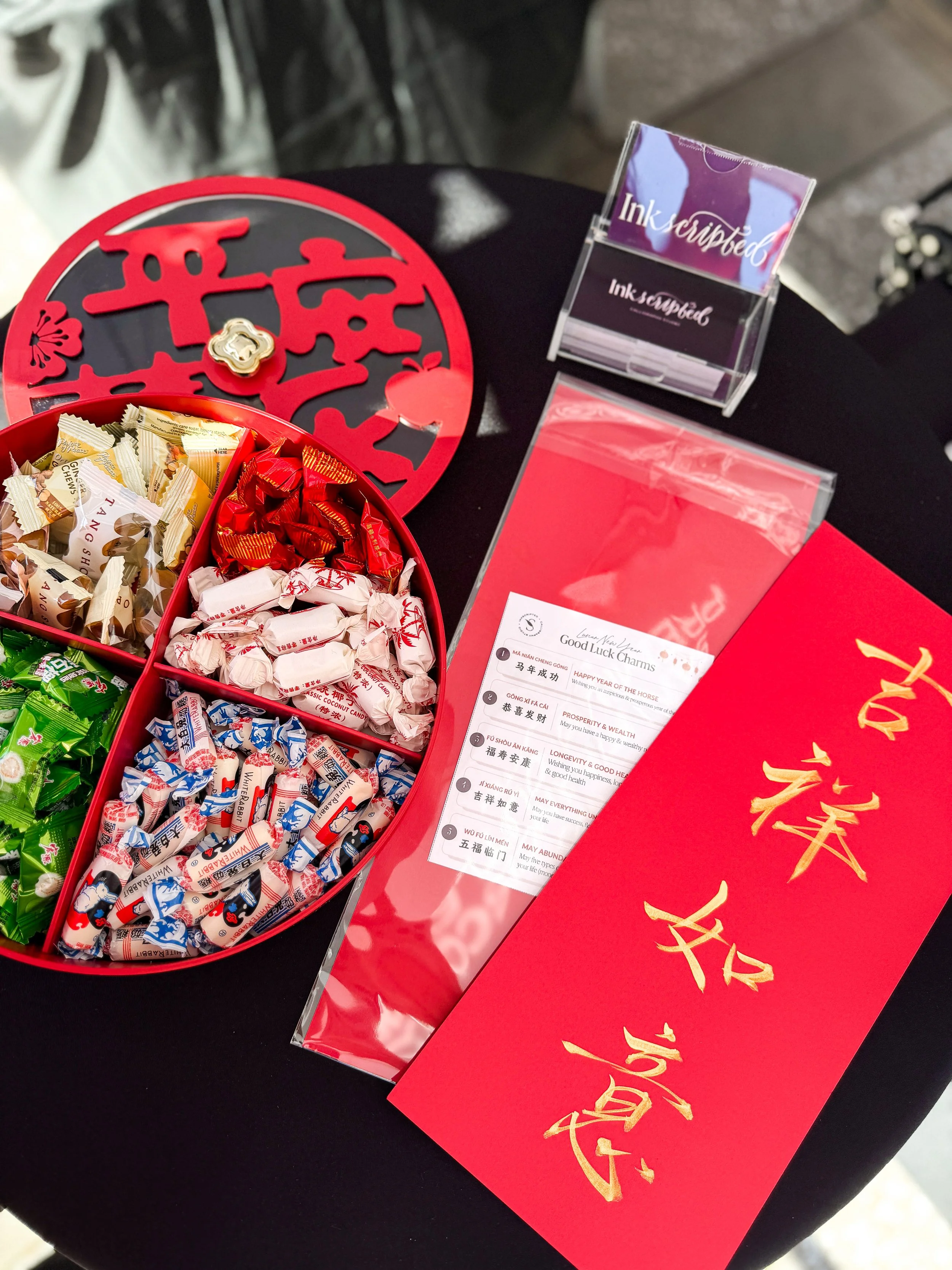 lunar-new-year-chinese-calligraphy-activation-simon-malls-livermore-premium-outlets-san-francisco-bay-area-brand-event-giveaway-cultural-gifting-aapi-celebration-table-setup-gold-ink-red-paper-candies.JPG