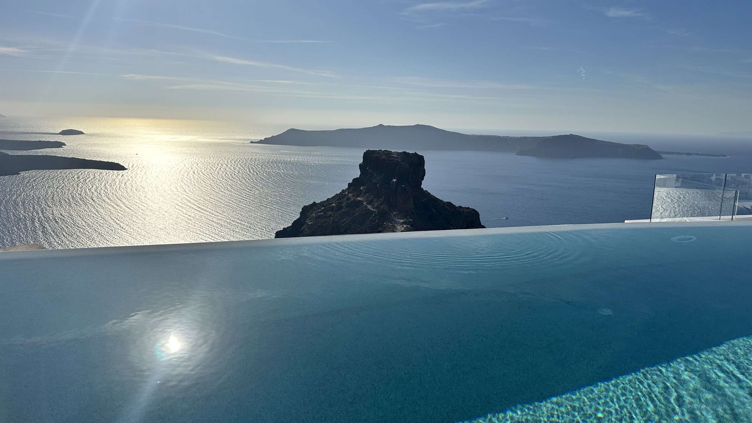 View of a large body of water with cliffs and islands in the distance, seen from a swimming pool or hot tub with a glass barrier.