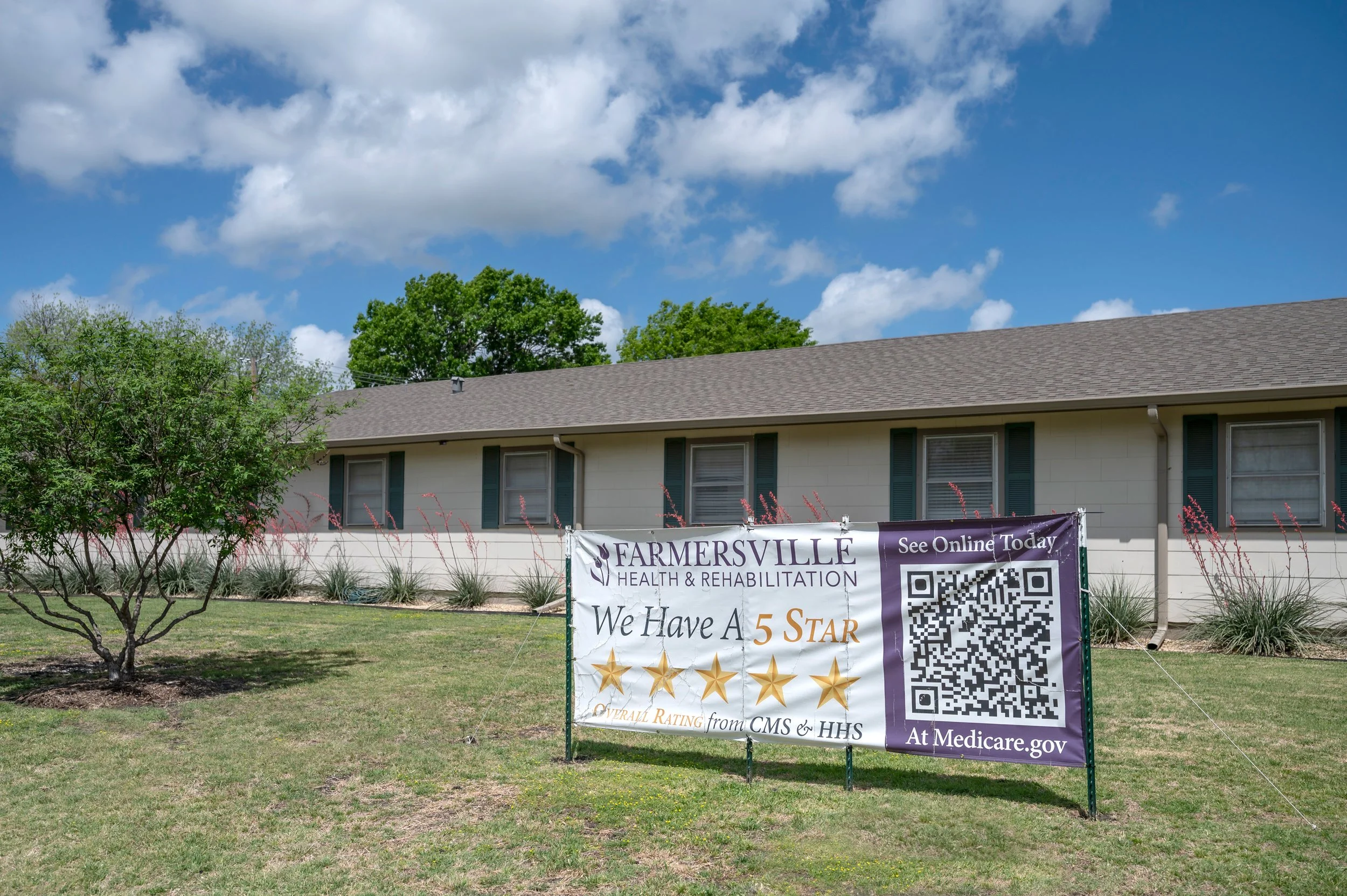 A large sign promoting Farmersville Health & Rehabilitation with a 5-star rating from CMS & HHS, a QR code, and a website, placed on a lawn in front of a one-story building under a partly cloudy sky.
