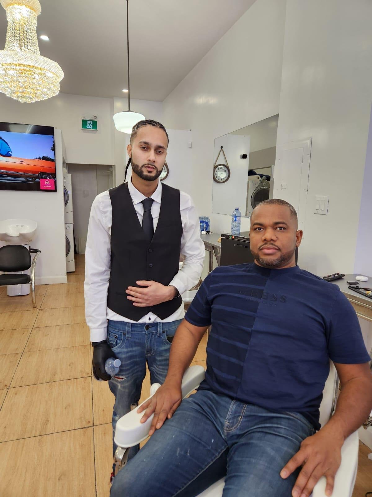 A man sitting in a barber chair with a barber standing beside him in a barbershop.
