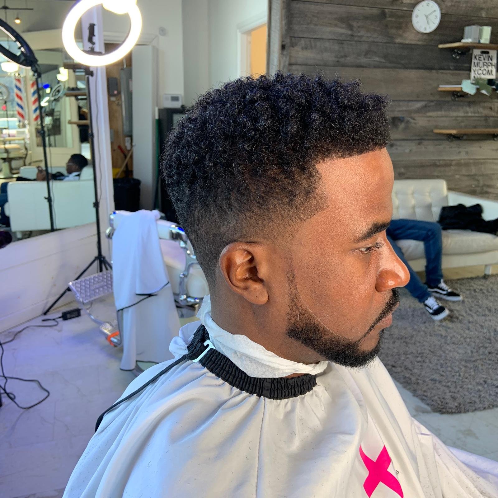 Man with a curly fade haircut sitting in a barber shop.