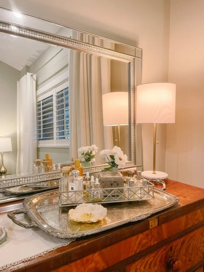 Vanity dresser with mirror, decorative lamp, and perfume bottles on silver tray