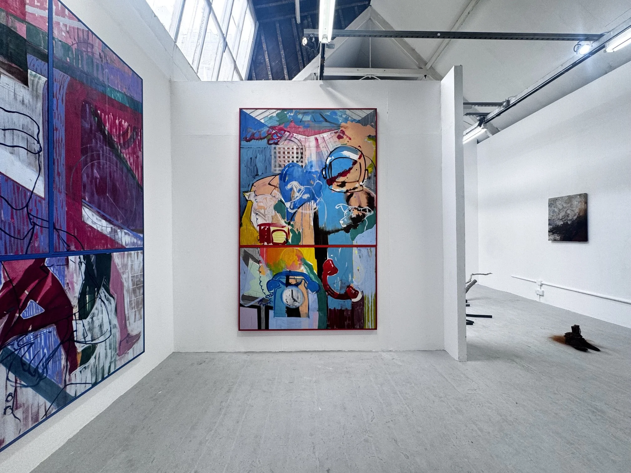 Interior of an art gallery with several colorful abstract paintings on white walls, skylights, and fluorescent lighting.