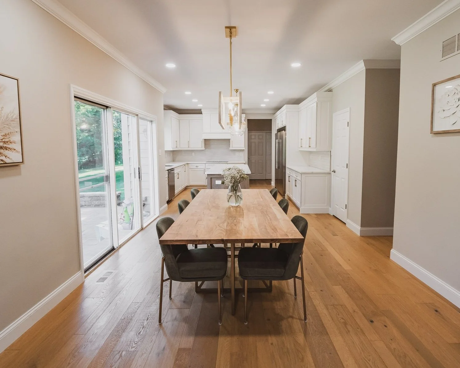 A gorgeous kitchen remodel with light wood flooring and long dinning table leading to an all white kitchen