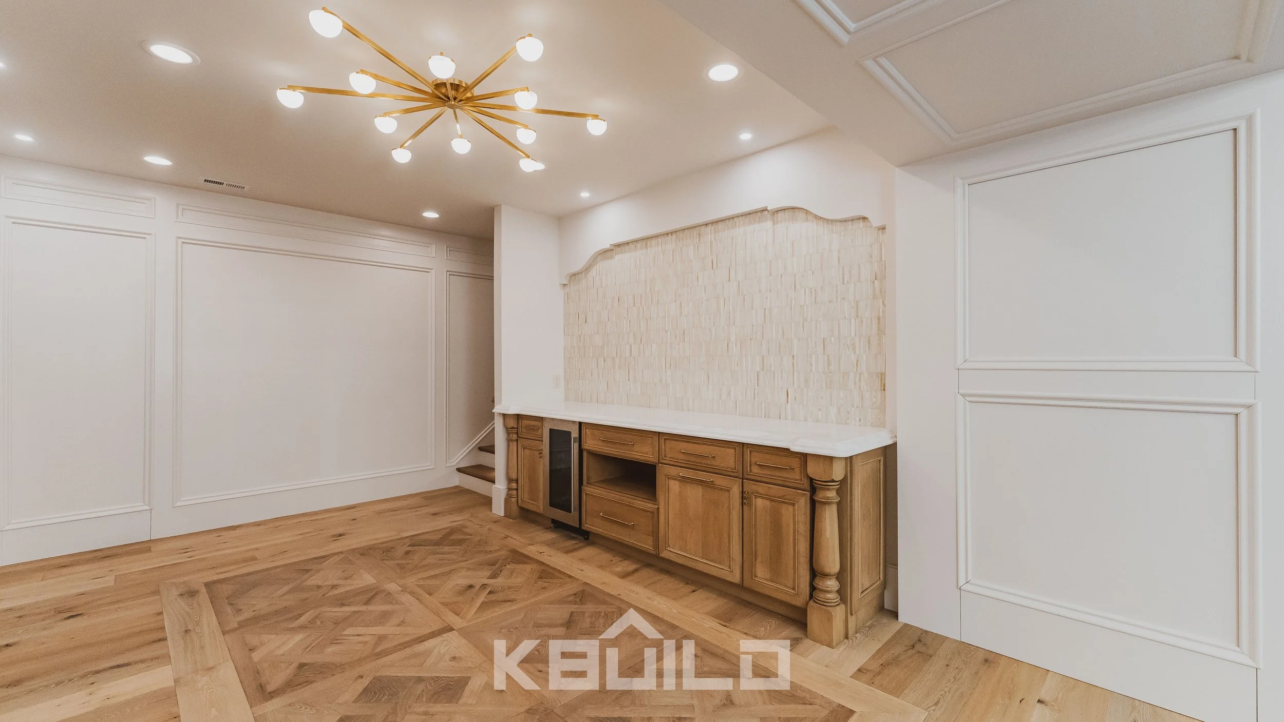 Elegant custom home bar with built-in cabinetry, patterned wood floors, designer lighting, and textured tile backsplash wall.