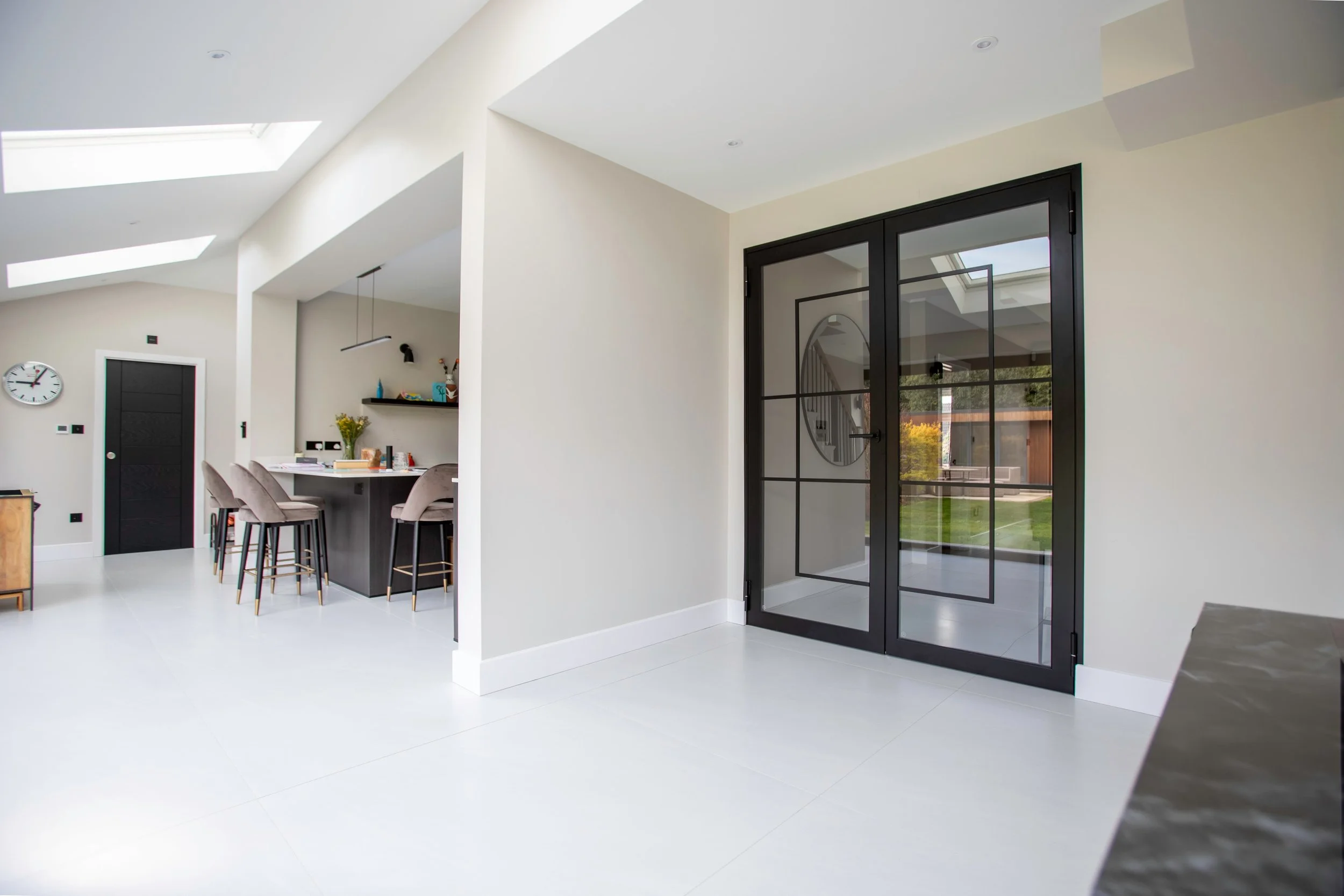 Fire-rated black steel double doors with clear glass separating a bright modern kitchen and open-plan living area.