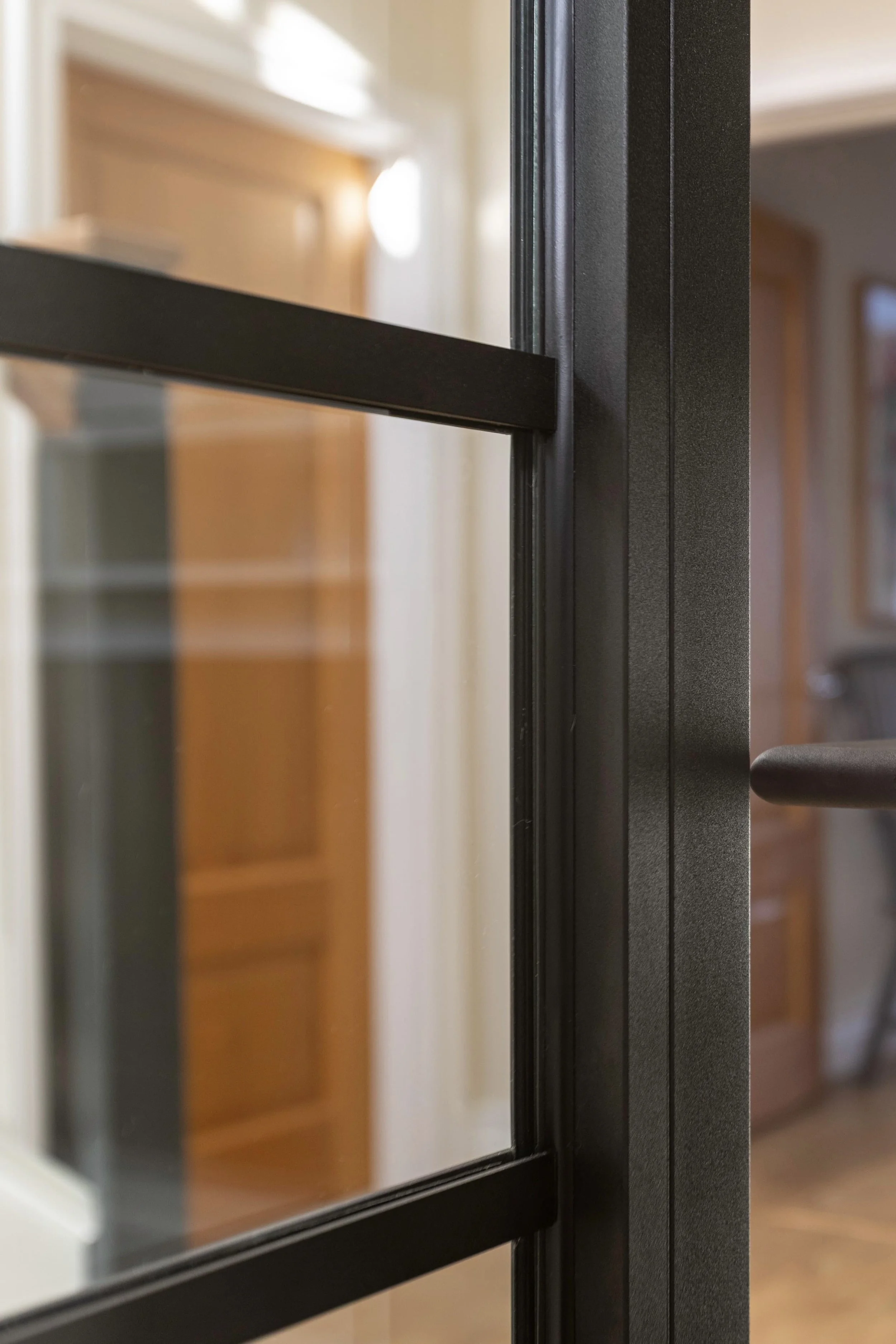 Detail of black internal steel door with horizontal bar and glass panel in modern residential interior.