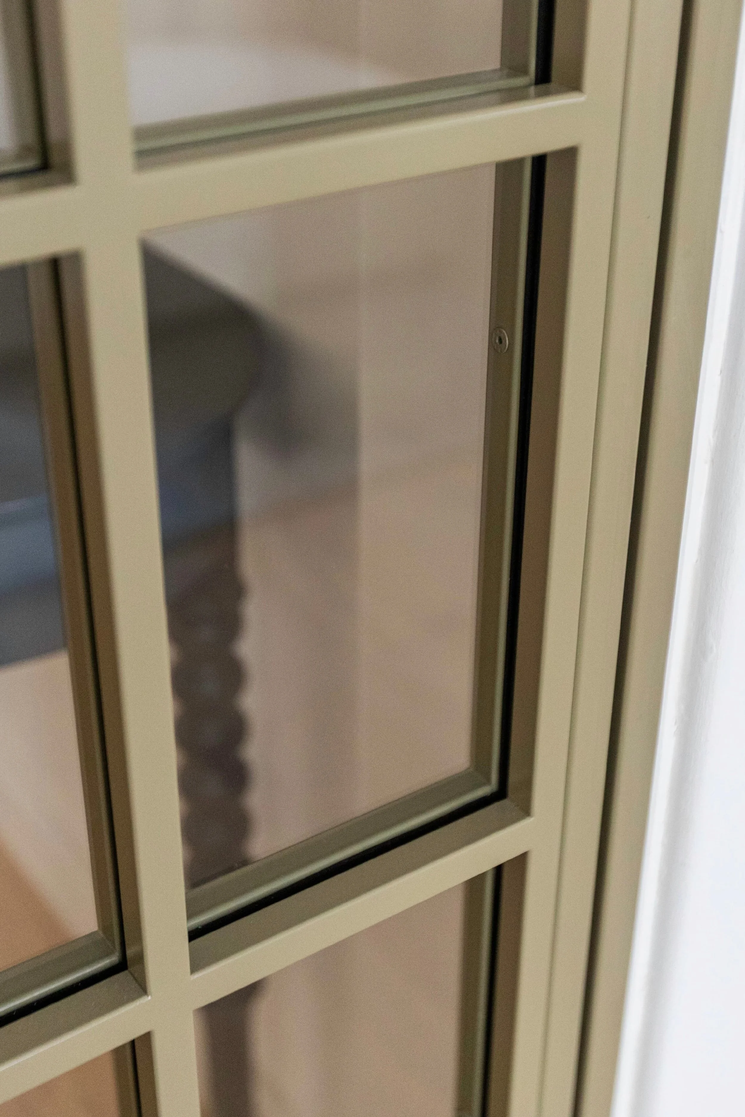 Close-up of olive grey steel door with horizontal bar detail and clear glass panel.