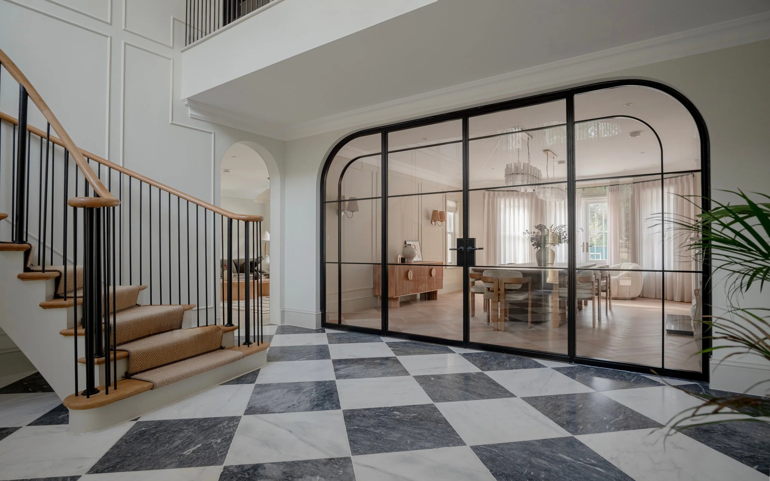 Bespoke InoCross20FR arched steel-framed fire-rated double doors with curved fixed side screens, viewed beside a sweeping staircase in a grand entrance hallway.