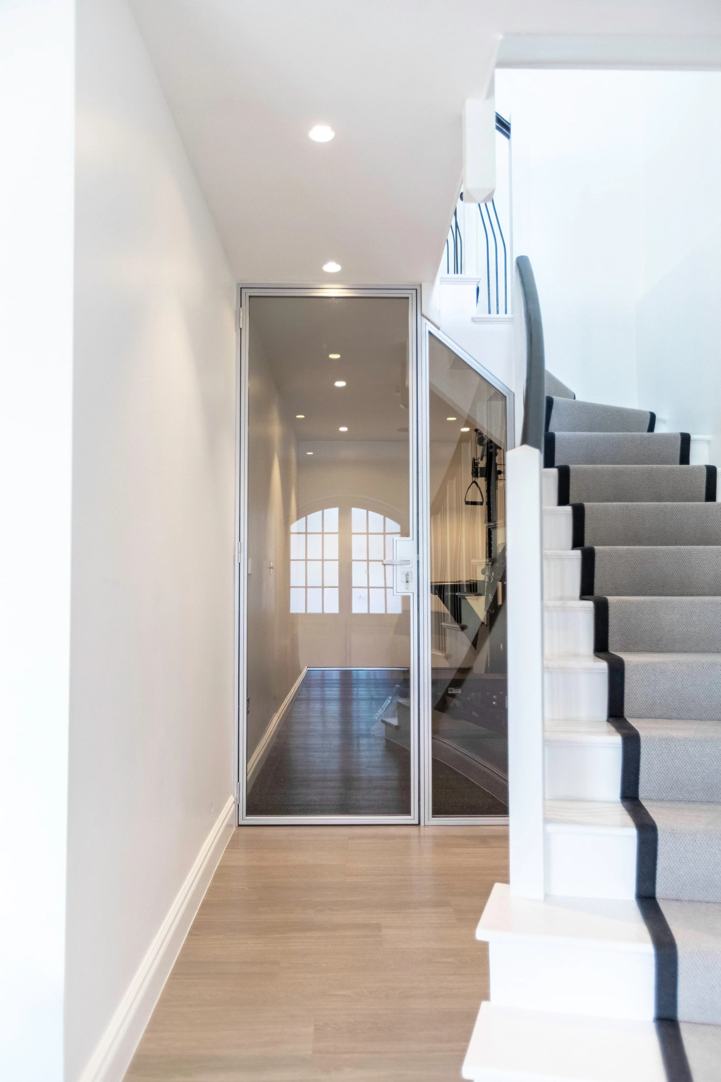 Bespoke steel glazed sliding door fitted beneath a staircase in a hallway, enclosing a home gym in a residential property in Highgate, London, installed by Joshua James.