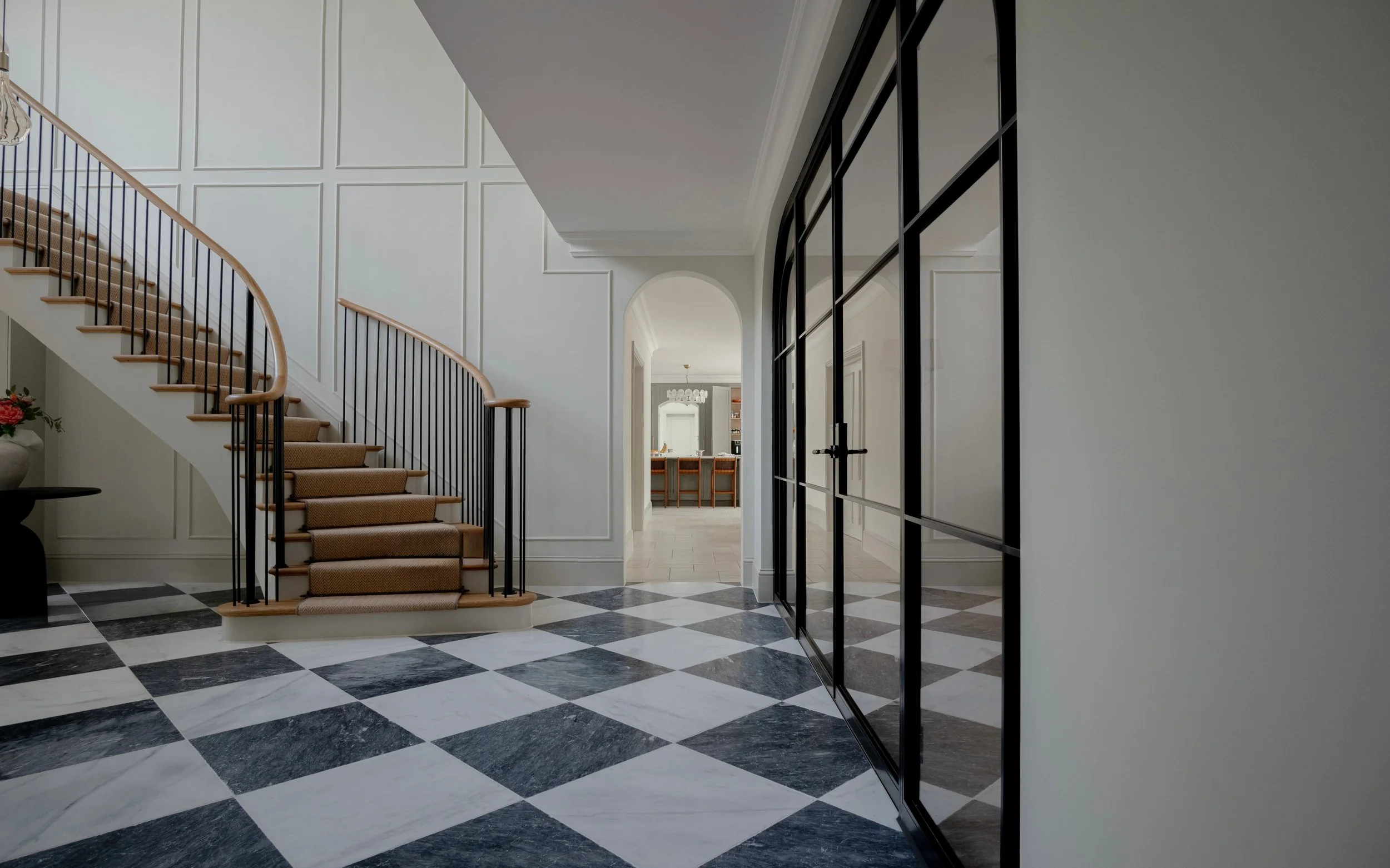 Side view of bespoke InoCross20FR arched steel-framed fire-rated double doors with glazed side screens, alongside a sweeping staircase and chequerboard marble flooring.