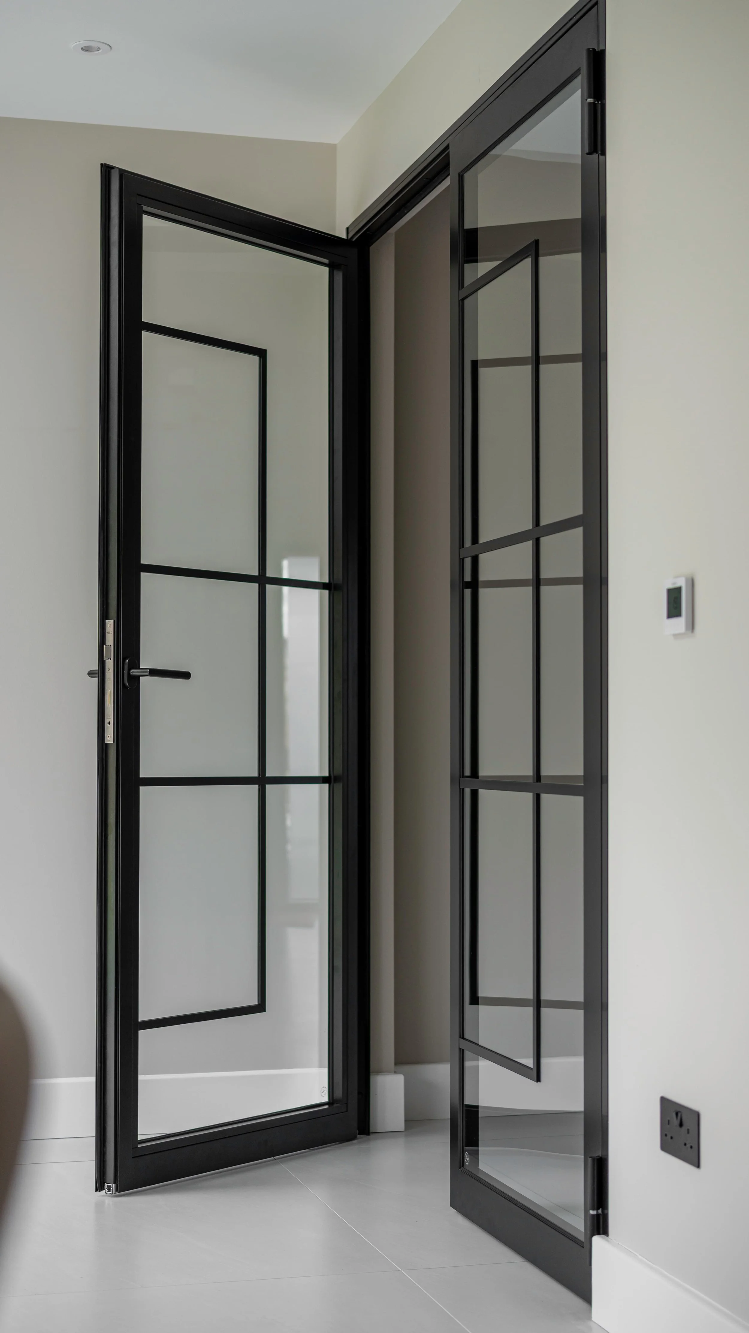 Modern black steel double doors with glazed panels in a minimalist interior, showcasing a sleek contemporary room divider design.