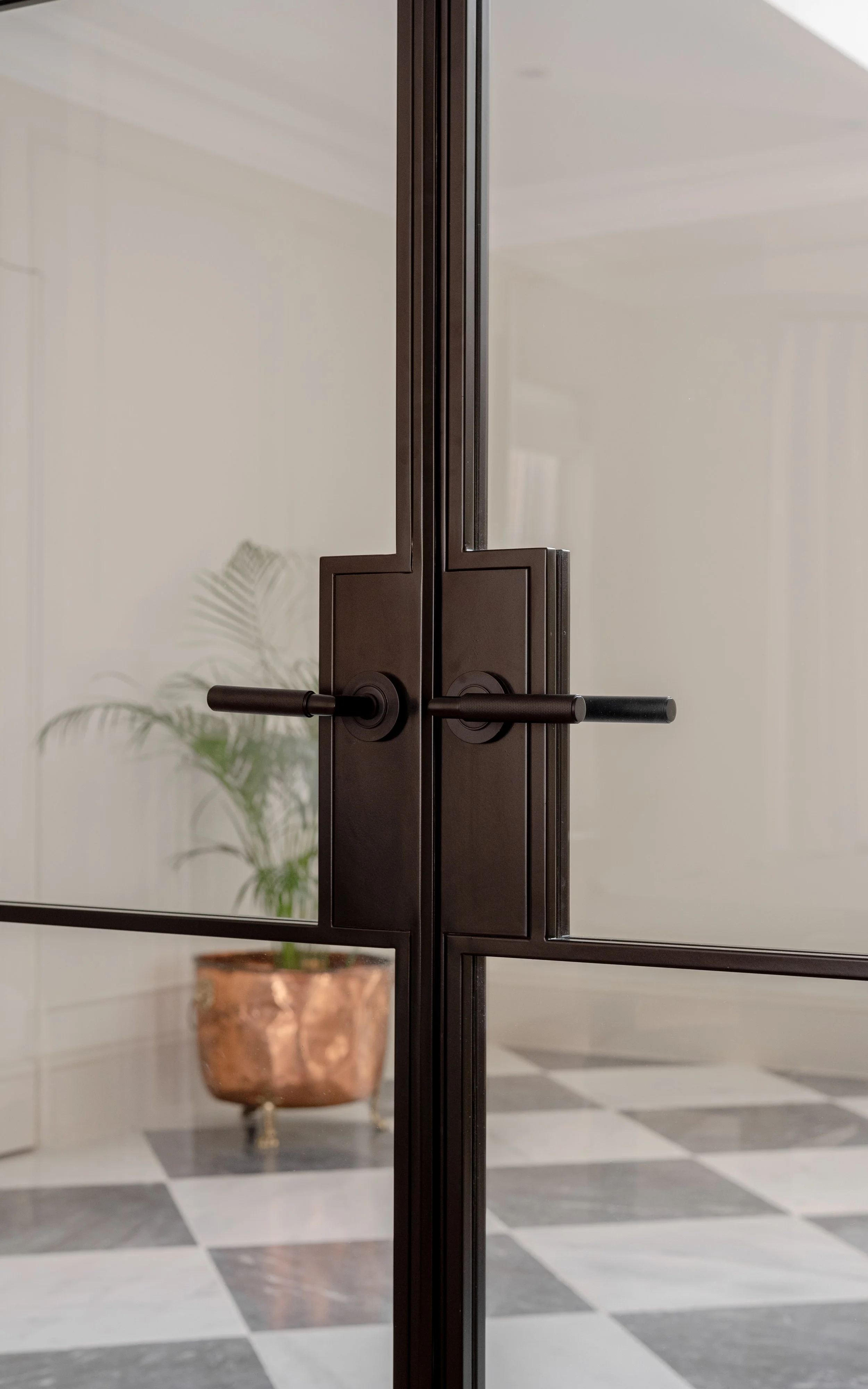 Close-up of bespoke InoCross20FR steel-framed fire-rated double doors, highlighting the matching dark bronze lever handles, slim steel profiles and glazed panels.