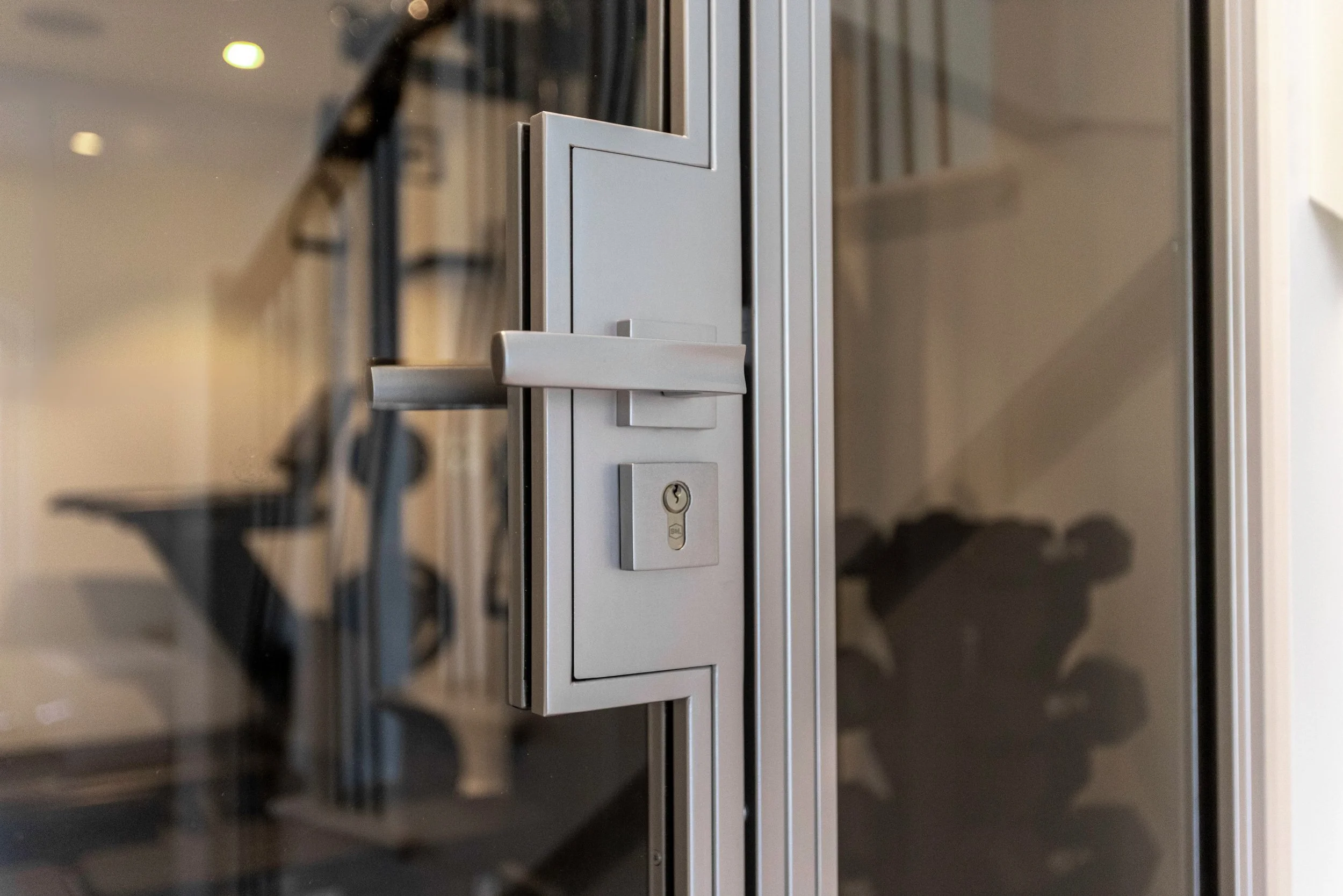 Close-up detail of brushed steel lever handle and lock on a bespoke steel glazed door enclosing a home gym in a residential property in Highgate, London, by Joshua James.