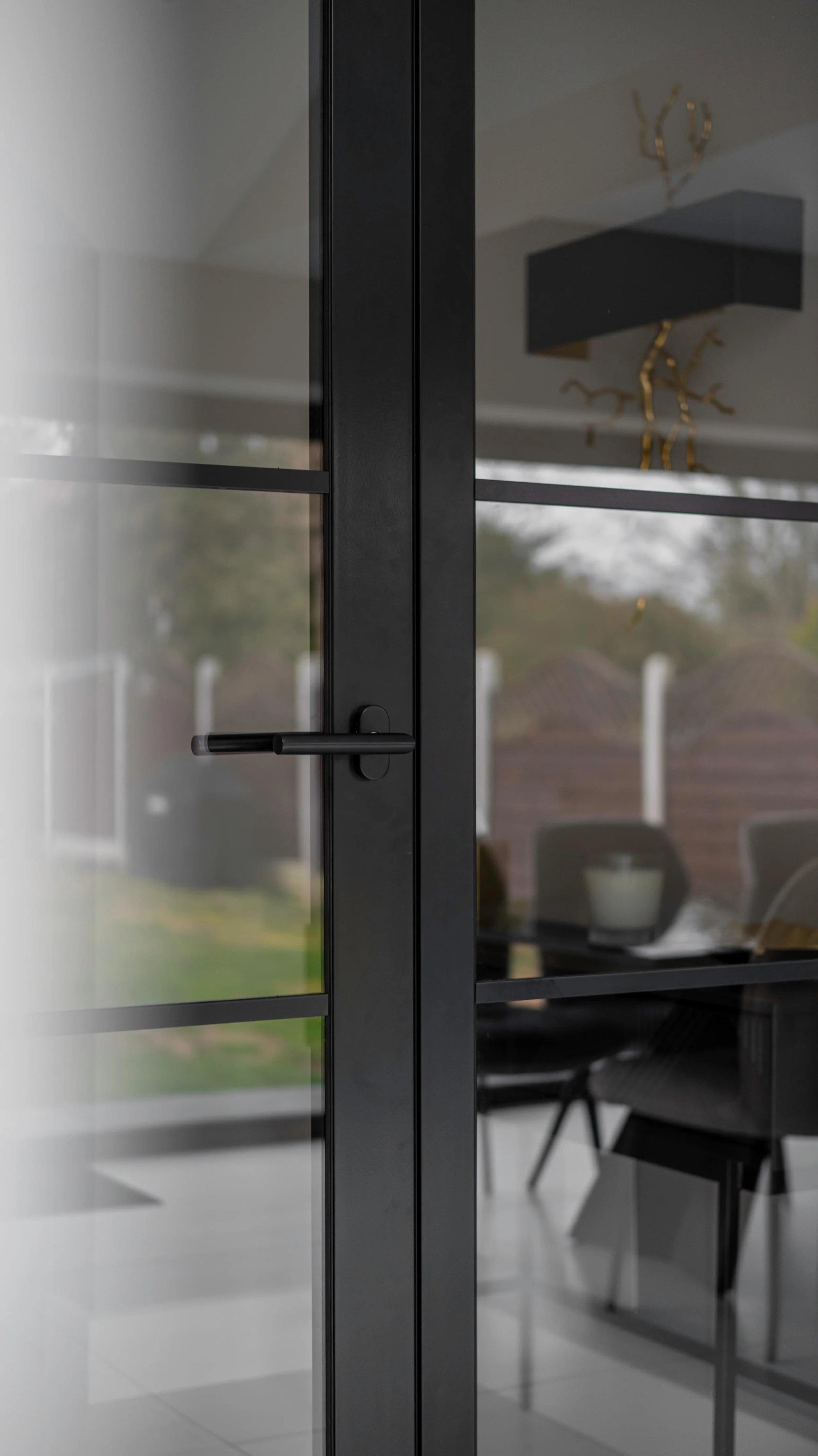Close-up detail of a black steel fire-rated door with minimalist black lever handle and clear glass panel.