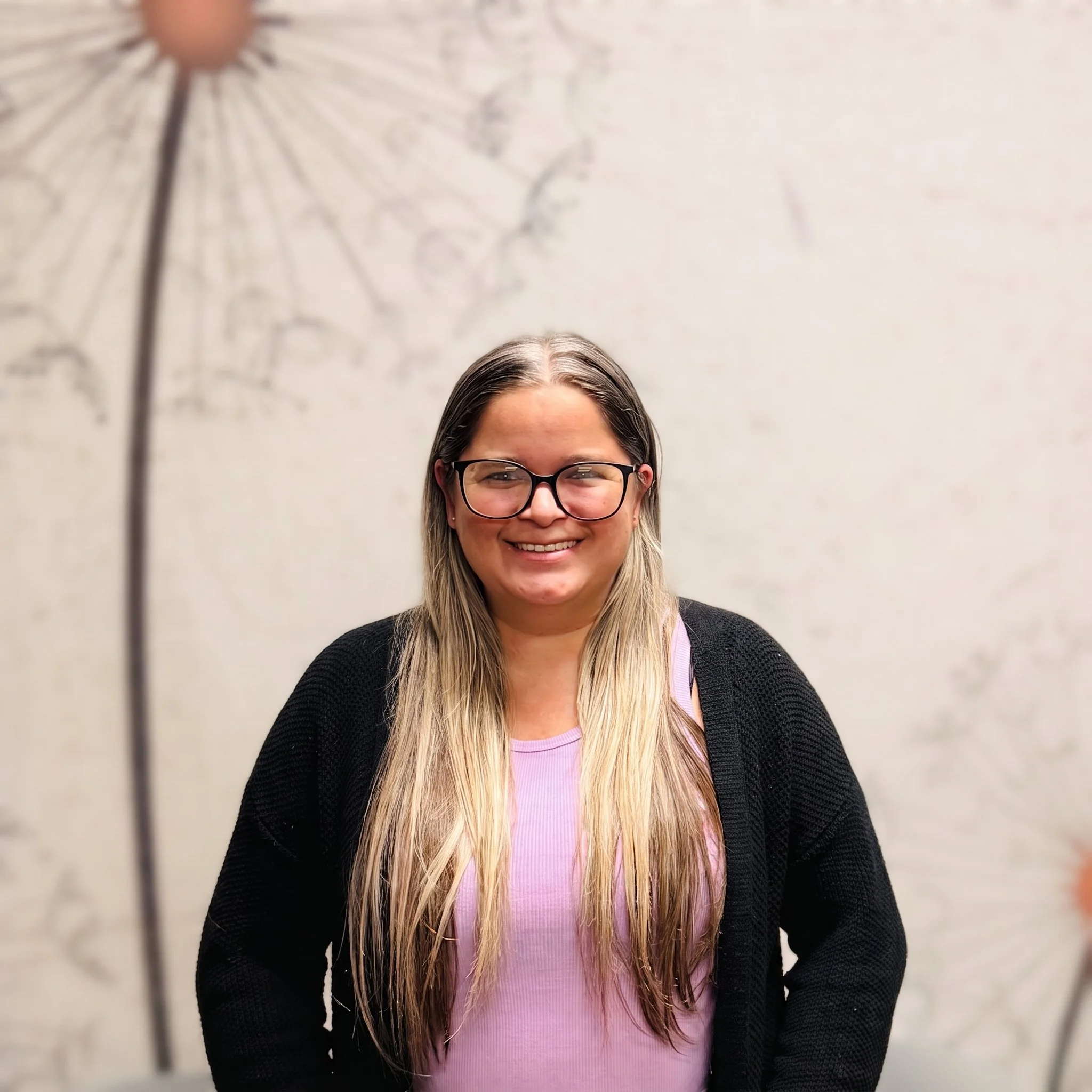 Alt Text: Keshia Torres, Billing Specialist at Dandelion Therapy Group in Florida, smiling in front of a dandelion wall backdrop.