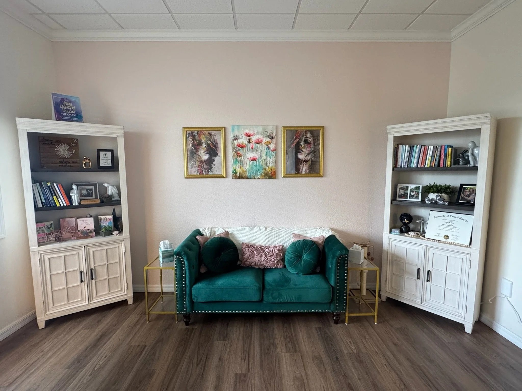 Elegant therapy space with a green velvet sofa, white bookshelves, and framed artwork at Dandelion Therapy Group in Punta Gorda.