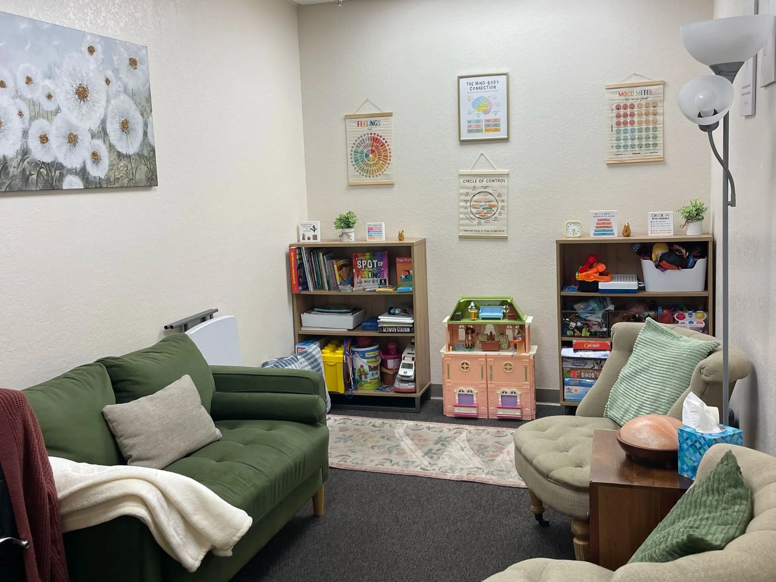 Equipped child play therapy and counseling room featuring a green sofa, toy dollhouse, and learning charts in Fort Myers.