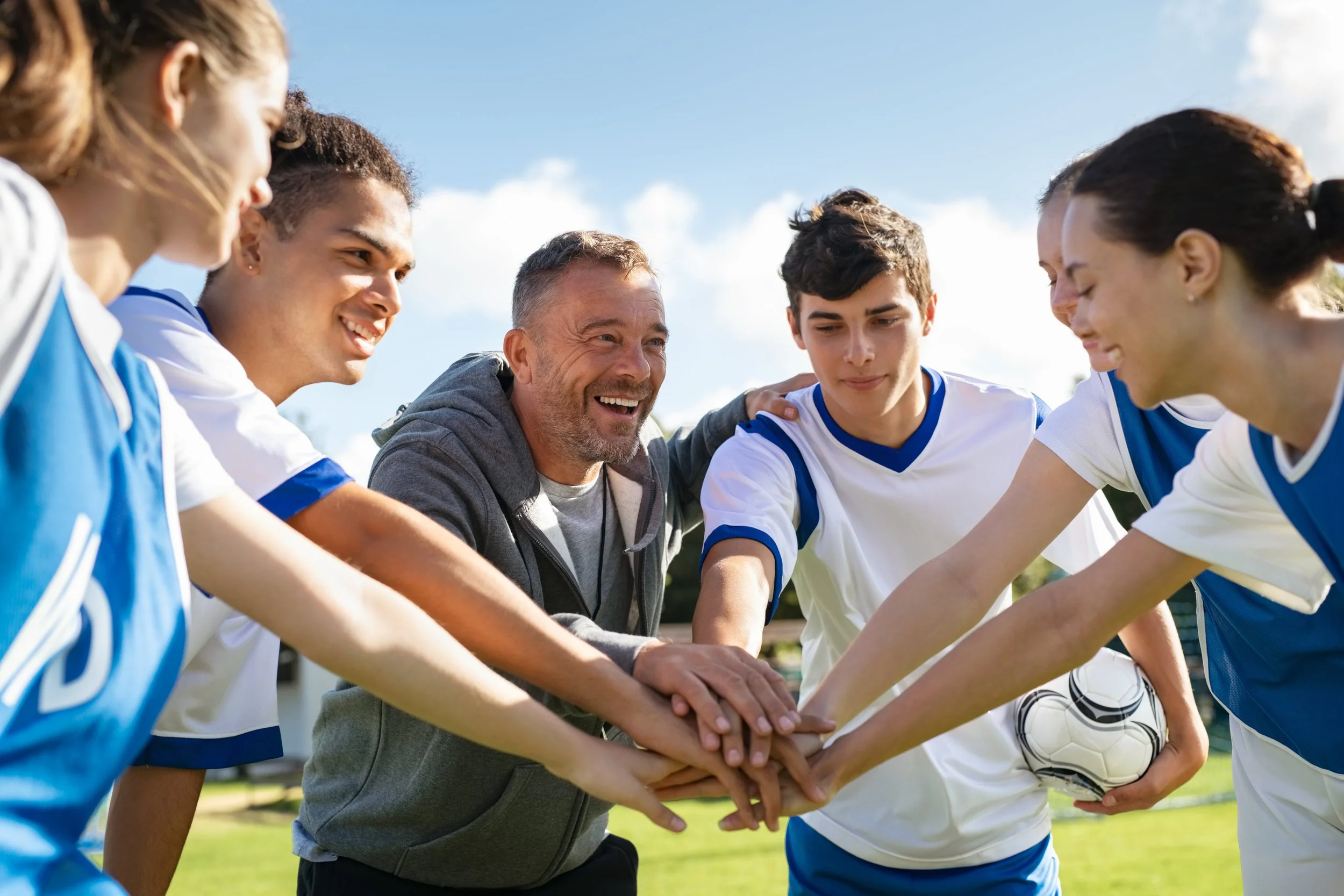 Soccer coach and team huddling with hands together outdoors