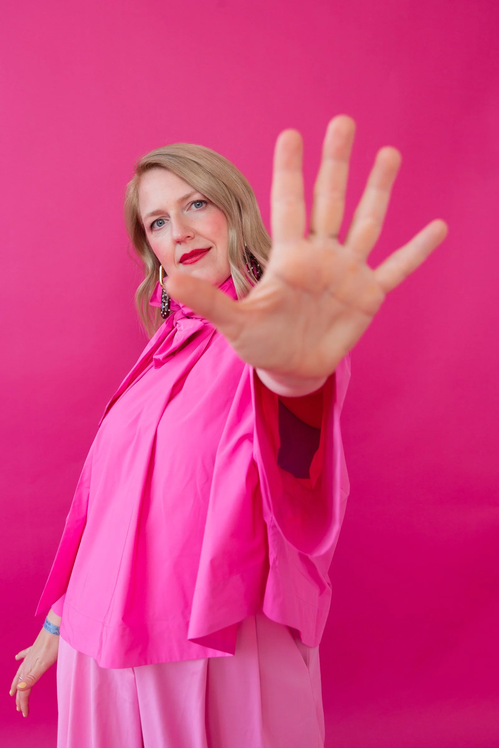 Farbige Frau in Pink, die die Kamera mit ausgestreckter Hand hält.