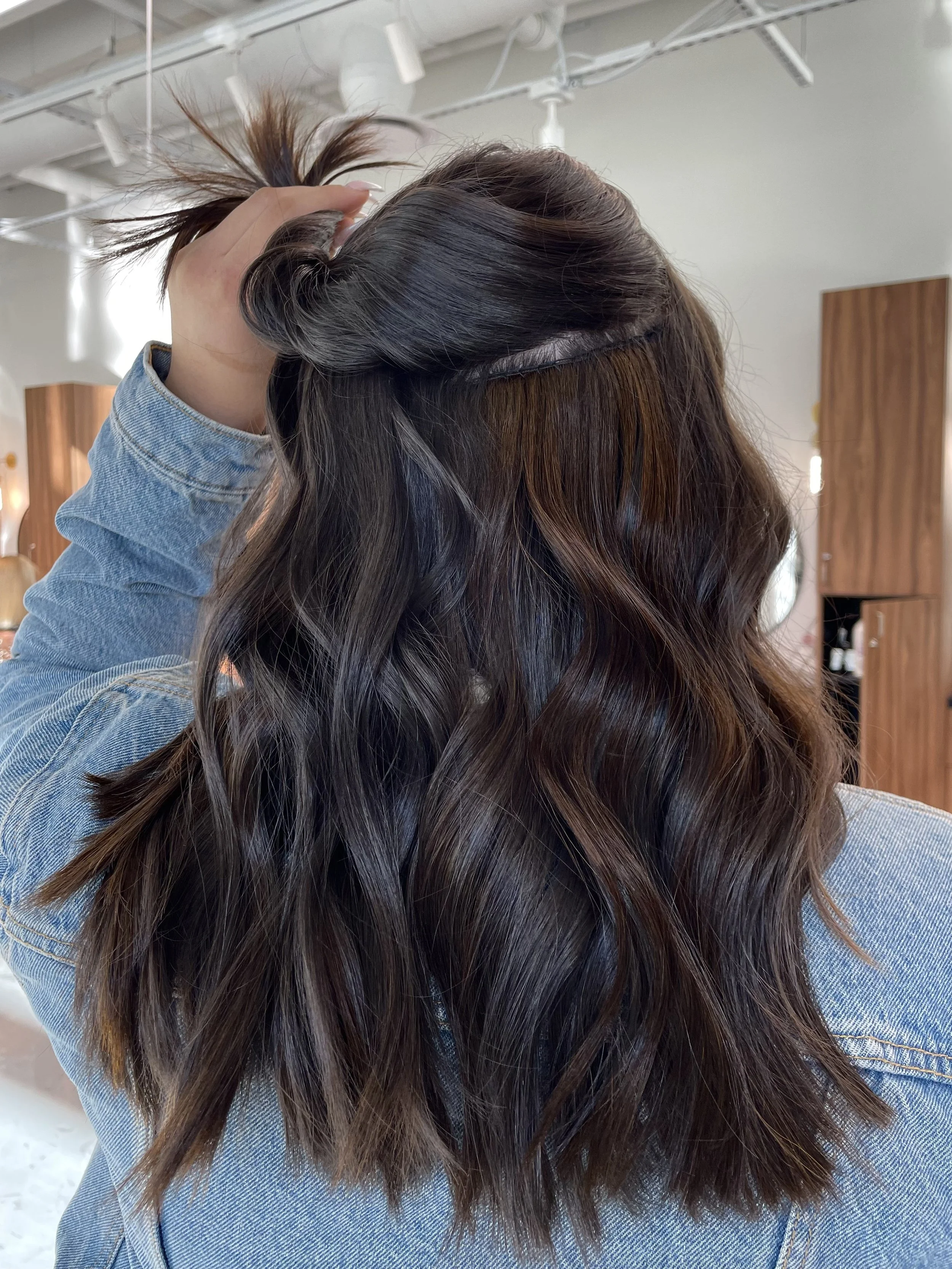 Client holding up a section of her hair to reveal weft extensions perfectly blended with her natural hair, demonstrating seamless length and blend at EVOQ Salon in Las Vegas.