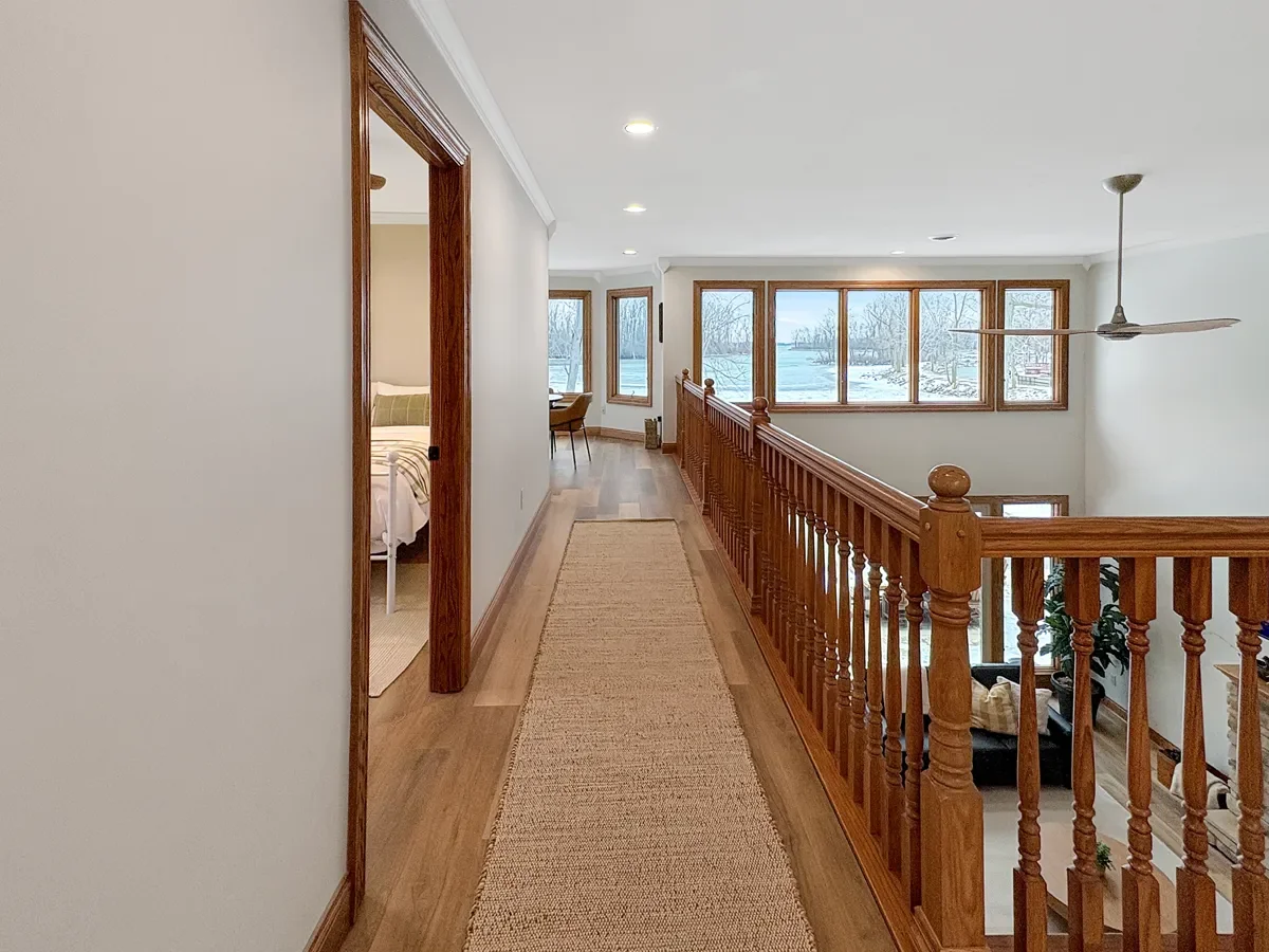 Hallway with hardwood floors, wooden railing, and large windows overlooking a snowy landscape.