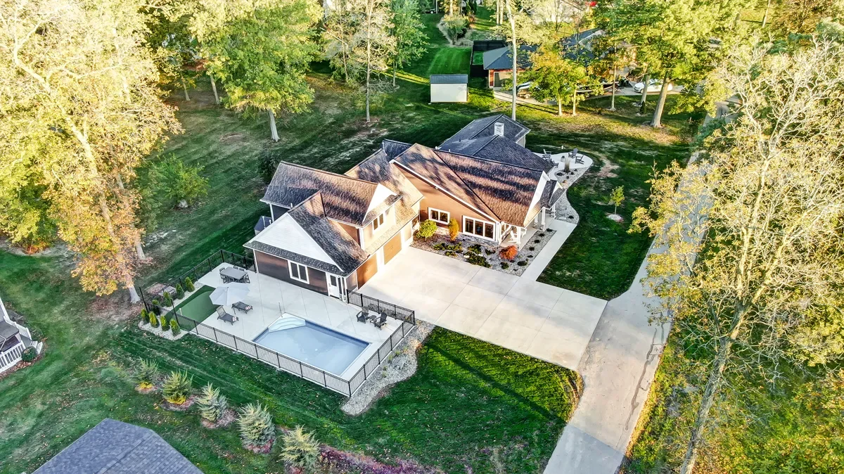 Aerial view of a house with a swimming pool, patio, and surrounding trees in a suburban neighborhood.