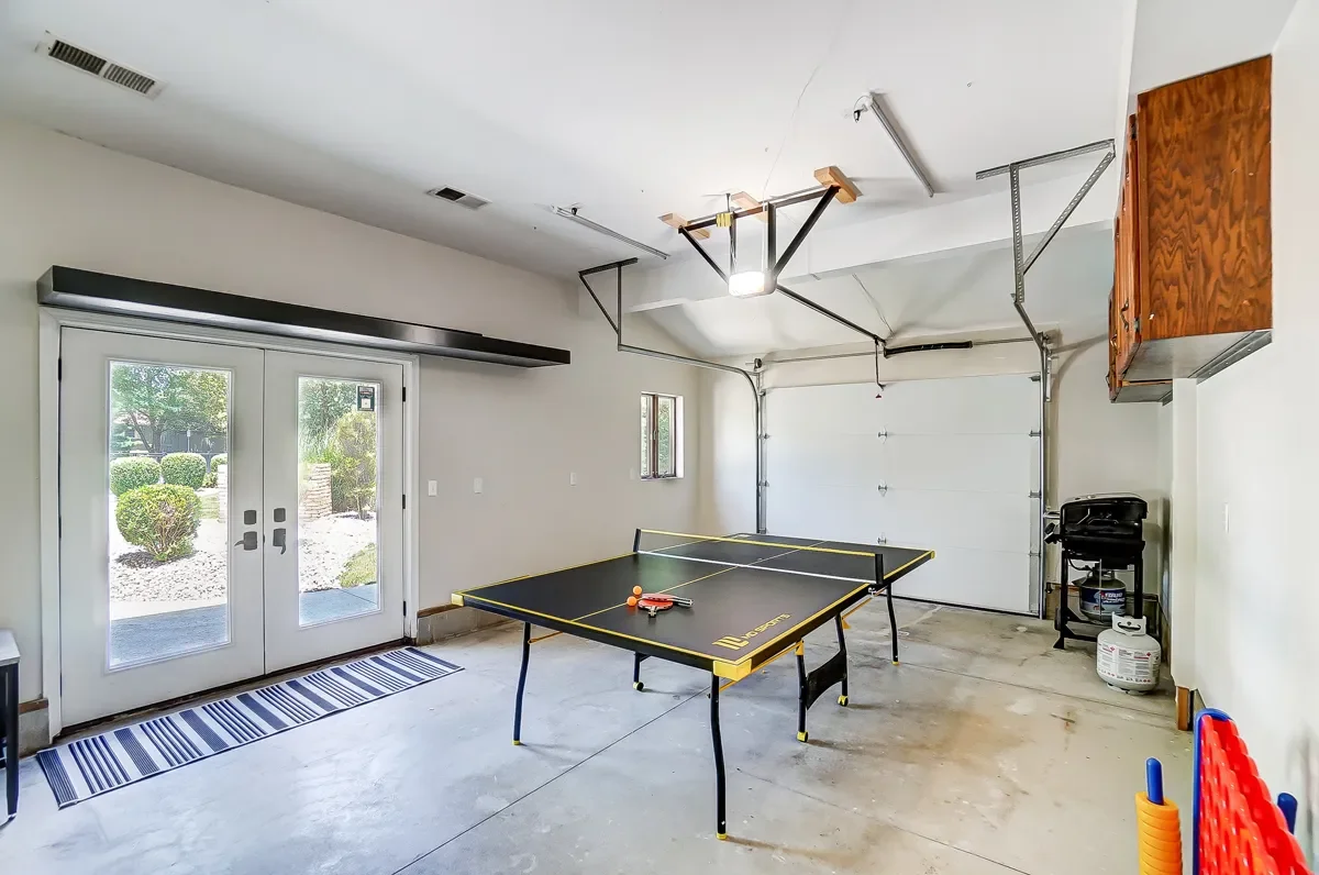 Garage with ping pong table, foldable garage door, small window, cabinet, propane tank, and outdoor view through glass double doors.