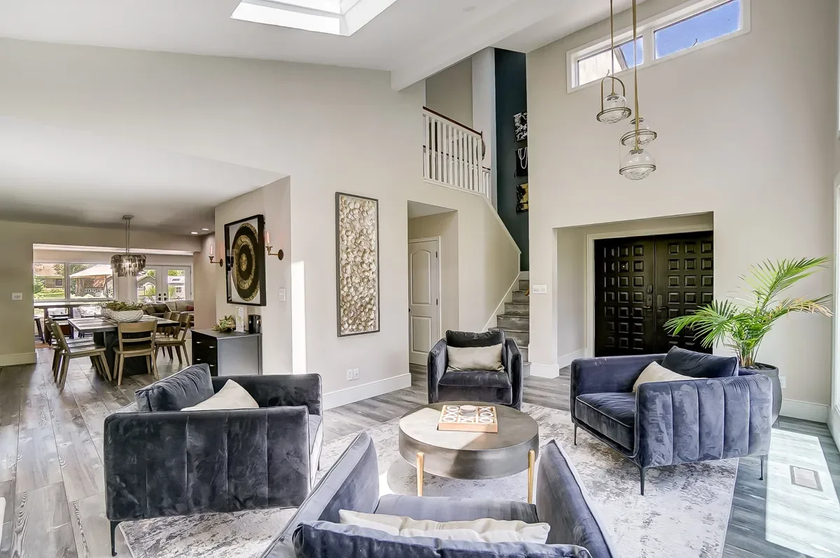 Modern living room with four navy velvet armchairs around a round coffee table, hardwood floors, and a large window letting in natural light.