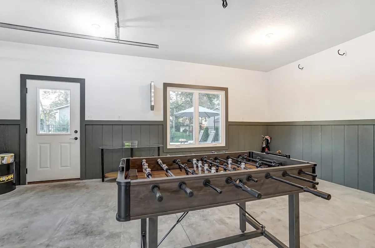 Empty game room with a foosball table, a door, a window showing an outdoor patio with an umbrella and chairs, and hooks on the wall.