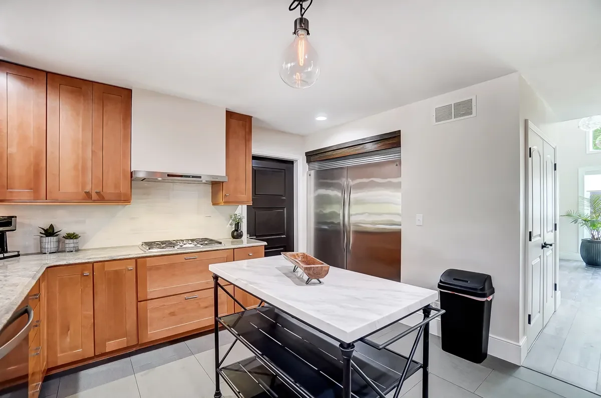 Modern kitchen with wooden cabinets, a marble-topped island, stainless steel refrigerator, black door, and minimalist decor.