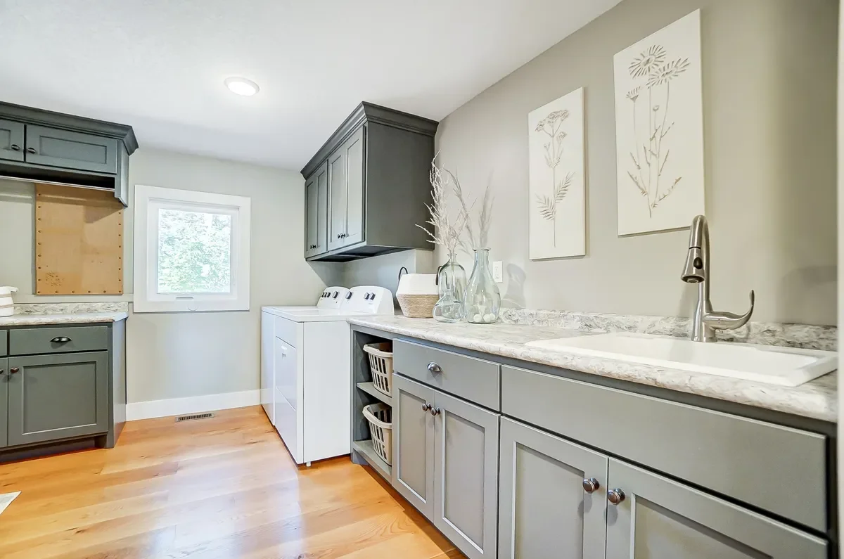 Kitchen with gray cabinets, a white laundry machine, a window, and wall art of botanical illustrations.